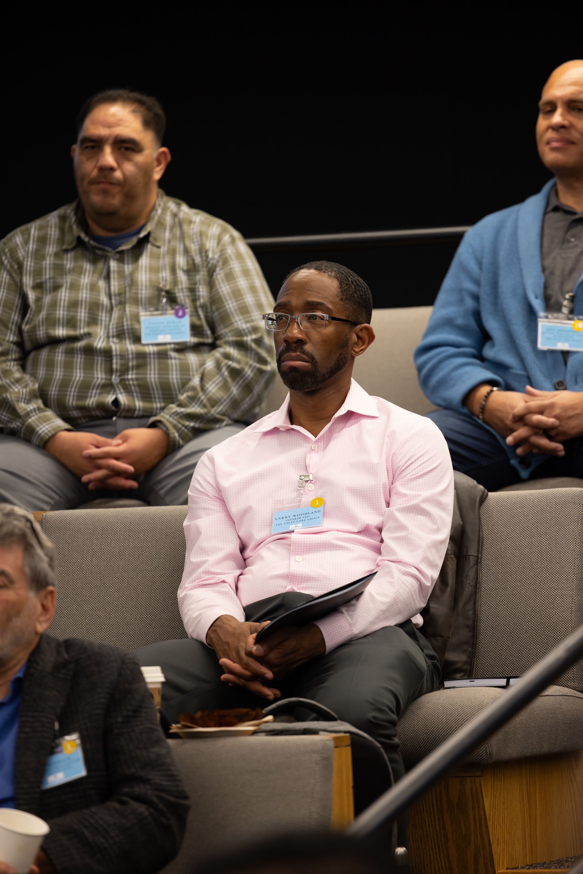 Audience members seated in a conference room, wearing name badges and listening attentively