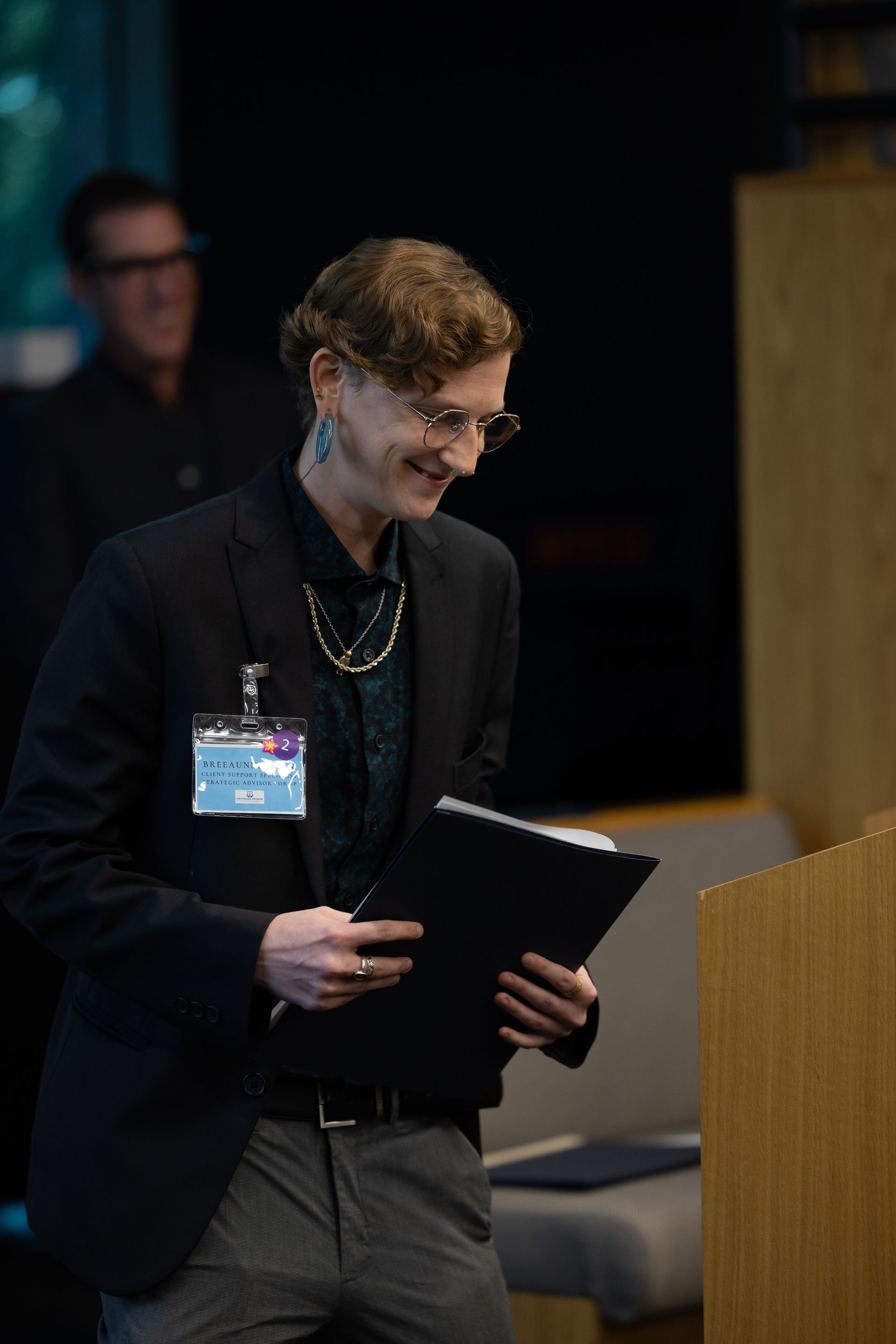 Person smiling and holding a clipboard at a podium during a presentation