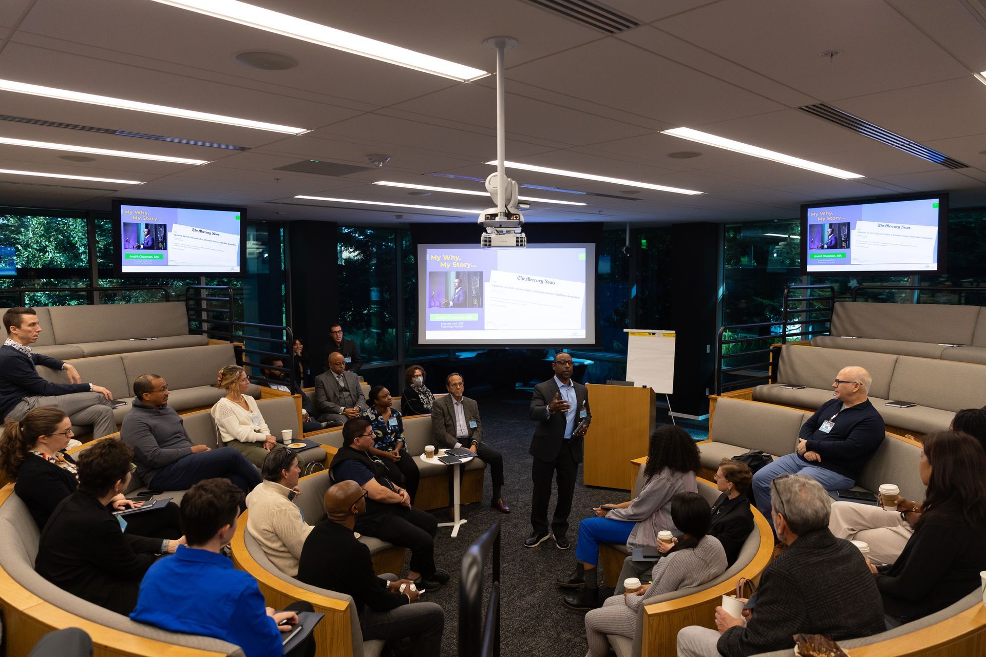 People seated in a conference room watching a presentation on a large screen.