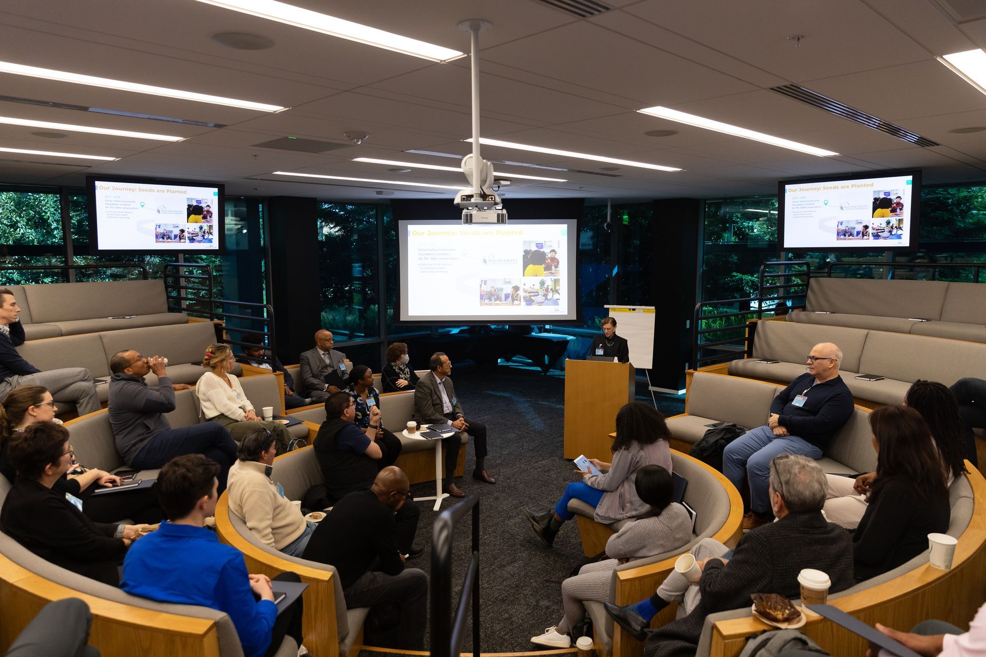 Audience seated in a conference room watching a presentation on two large screens