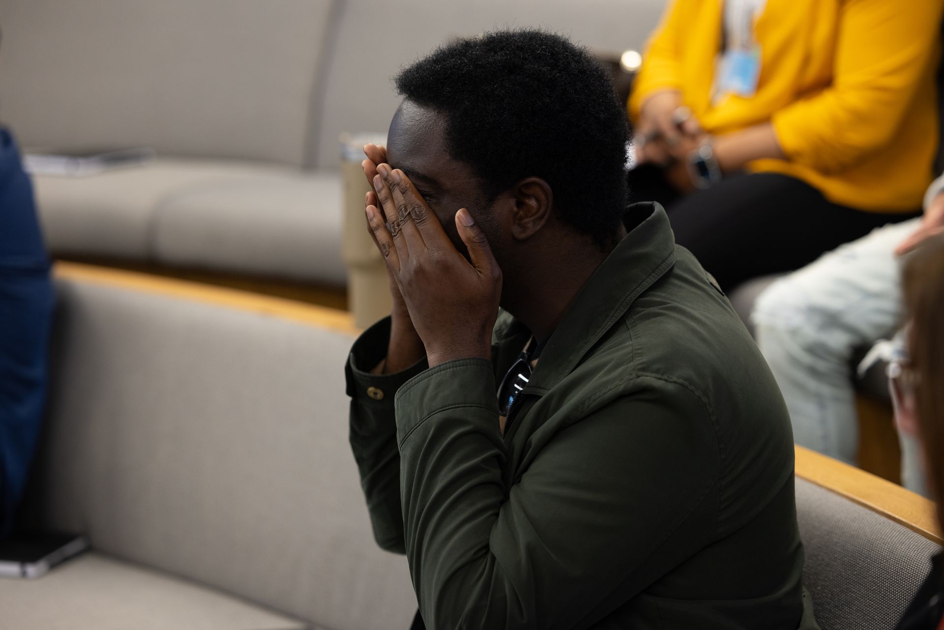 Person seated in a meeting room, covering their face with both hands.