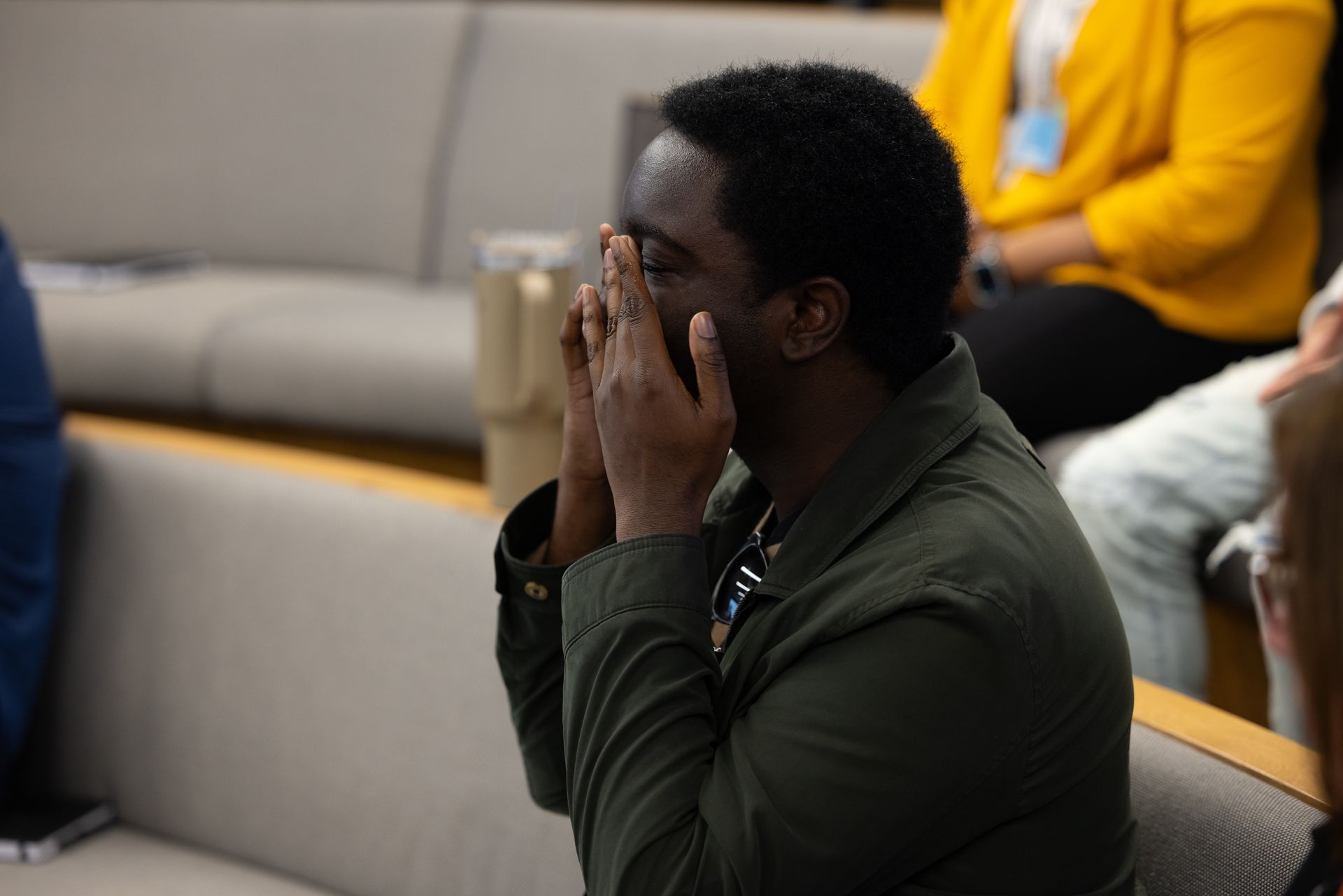 Man seated on a couch with hands covering his face in a modern lounge area