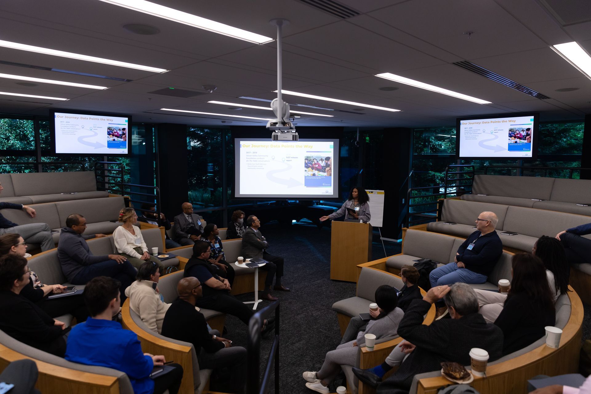 People seated in a conference room watching a presentation on large screens