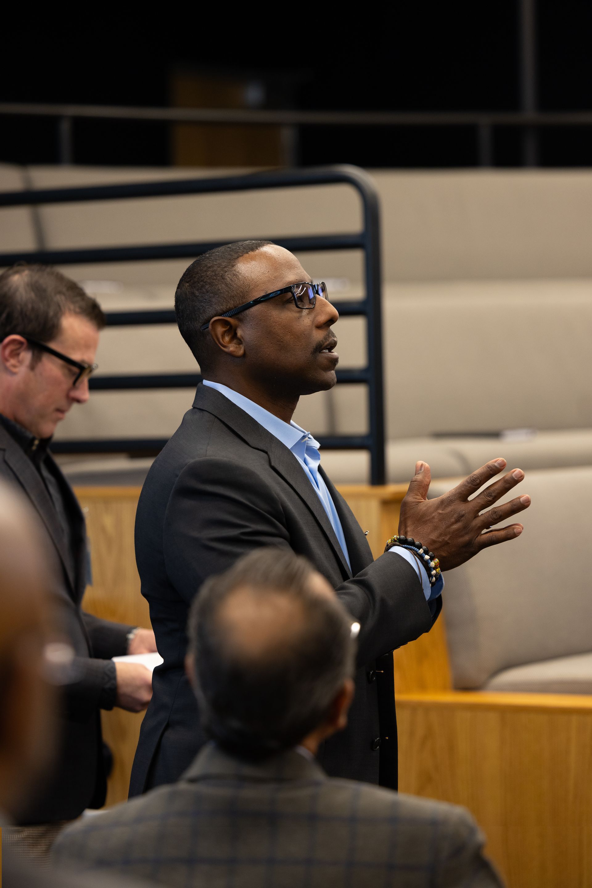 Man speaking in a courtroom, gesturing with hands while others sit nearby.