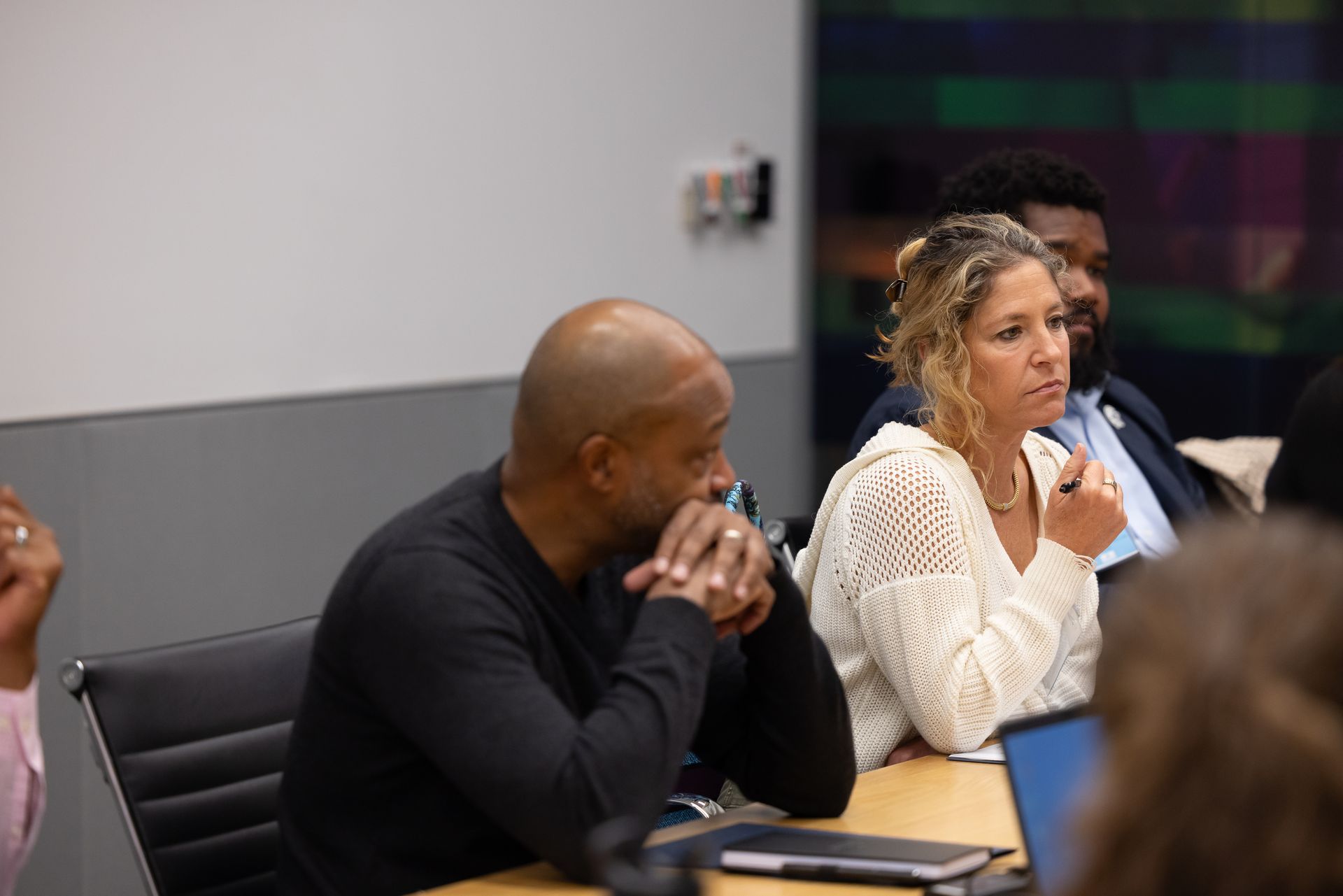 People seated at a conference table, listening attentively in a meeting room.