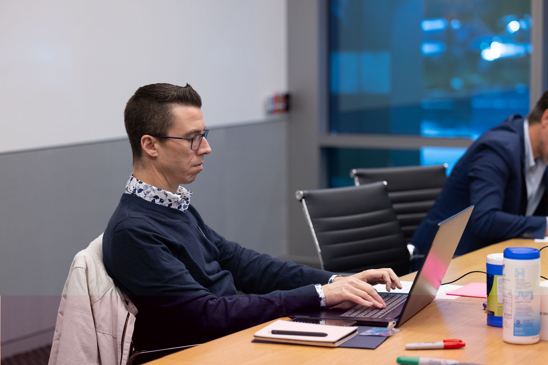 Person typing on a laptop at a conference table with notebooks and drinks in a meeting room