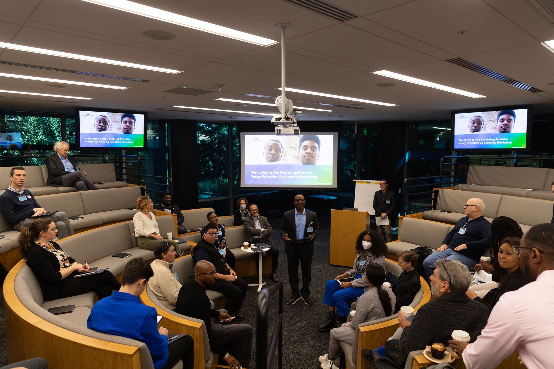 People seated in a conference room watching a video presentation on wall-mounted screens.