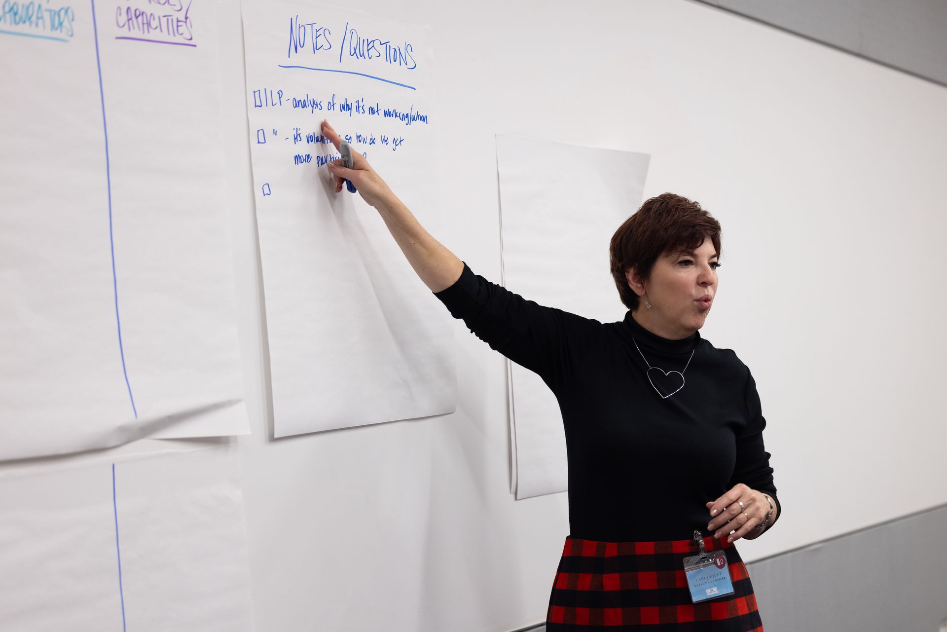 Presenter pointing at a whiteboard during a workshop, with notes and charts on the wall