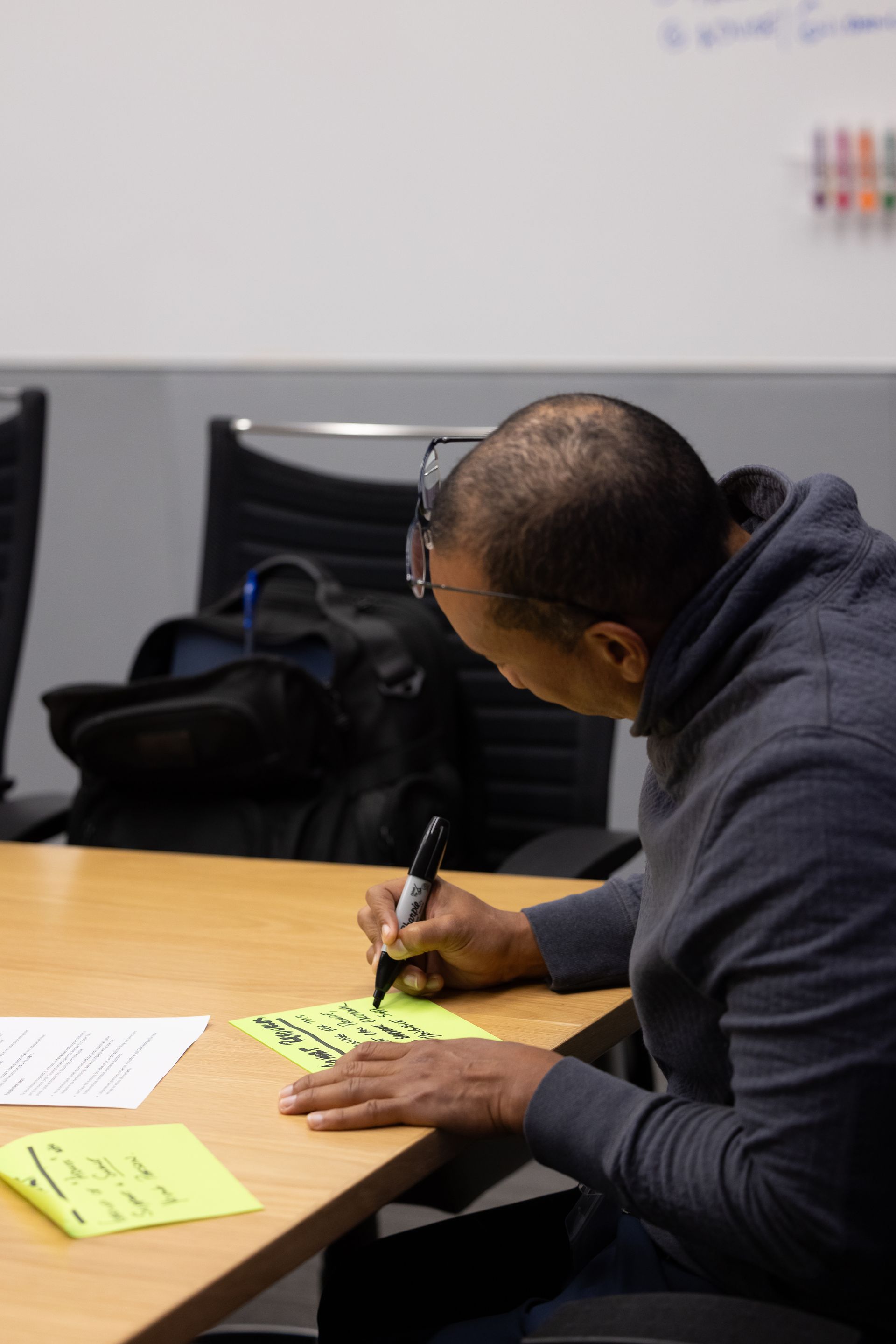 Person writing on a neon green note at a conference table in a meeting room