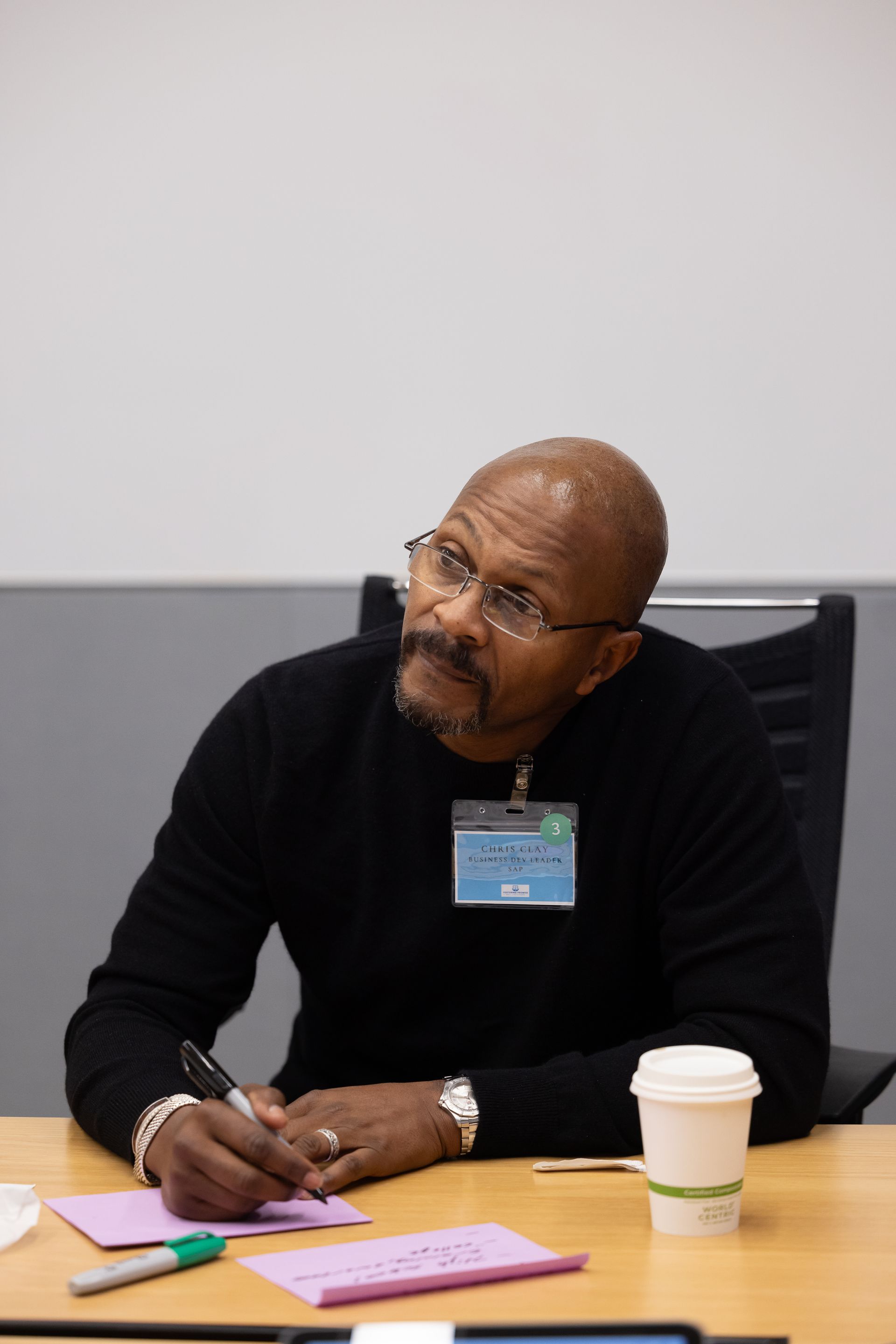 Man seated at a table, writing notes beside a coffee cup and papers, in a meeting room