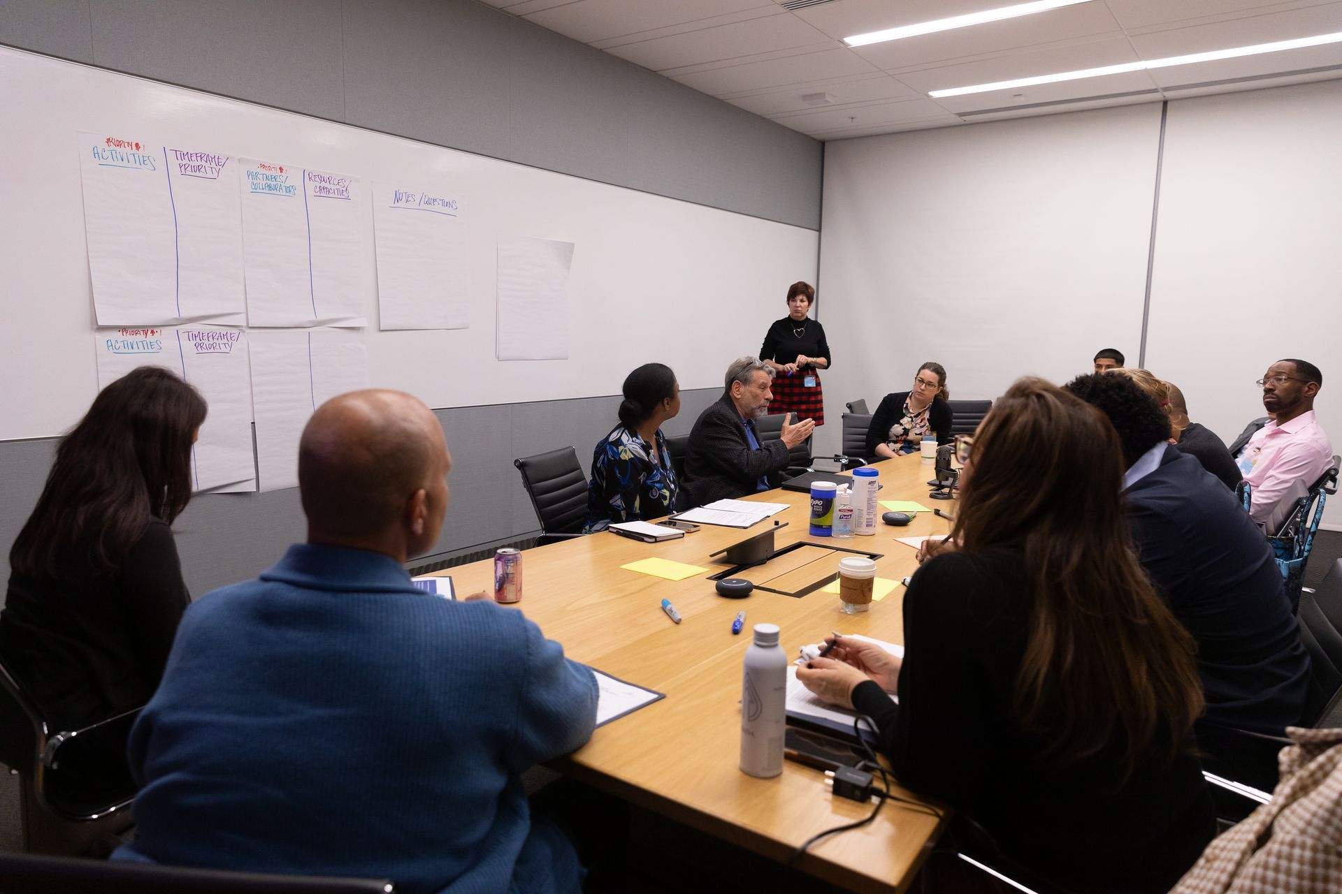 People seated around a conference table in a meeting room, discussing notes on a whiteboard.