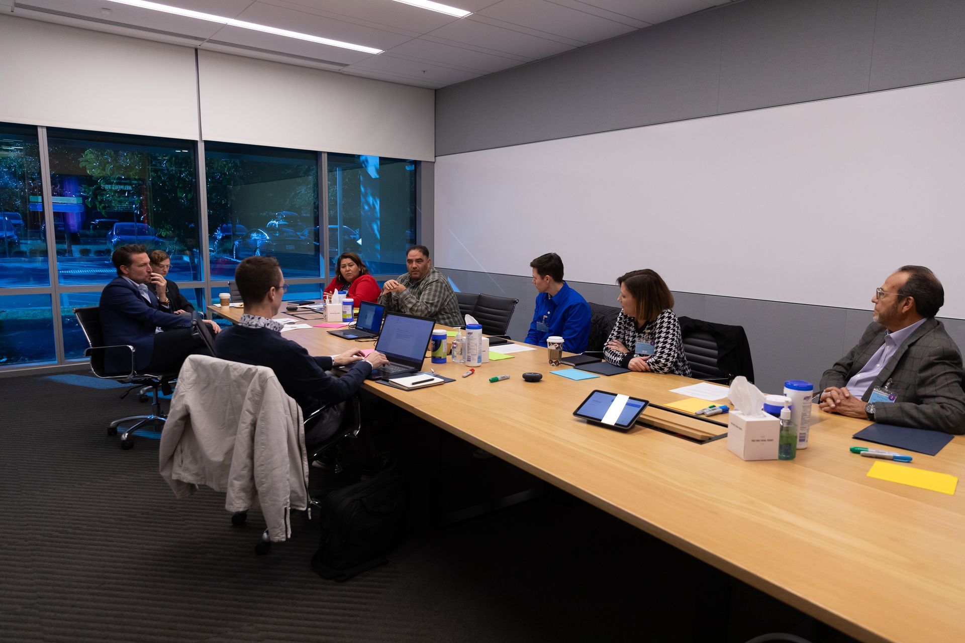 People seated around a conference table in a meeting room, with laptops, papers, and drinks.
