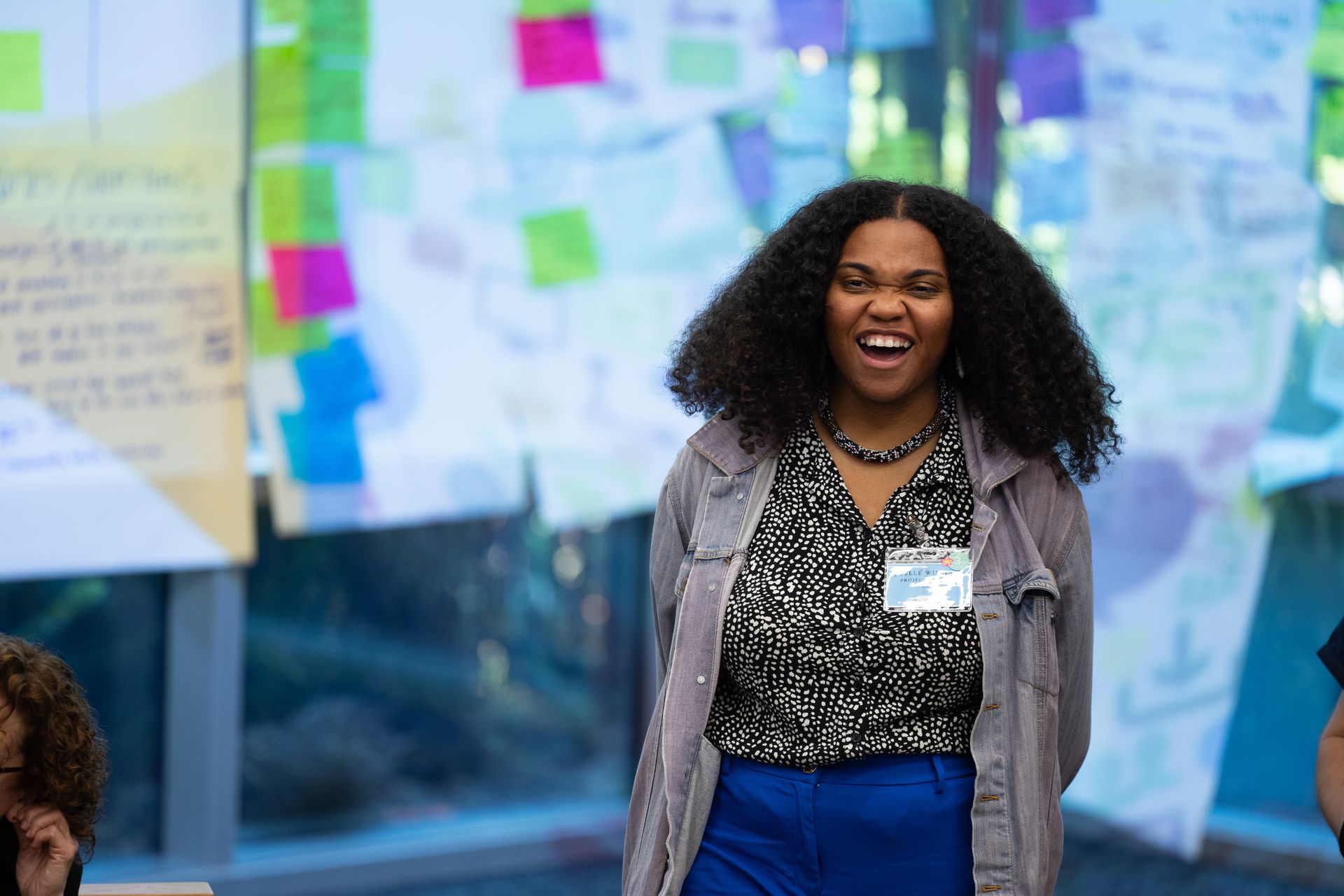 Smiling woman standing at a workshop with colorful sticky notes on the wall behind her