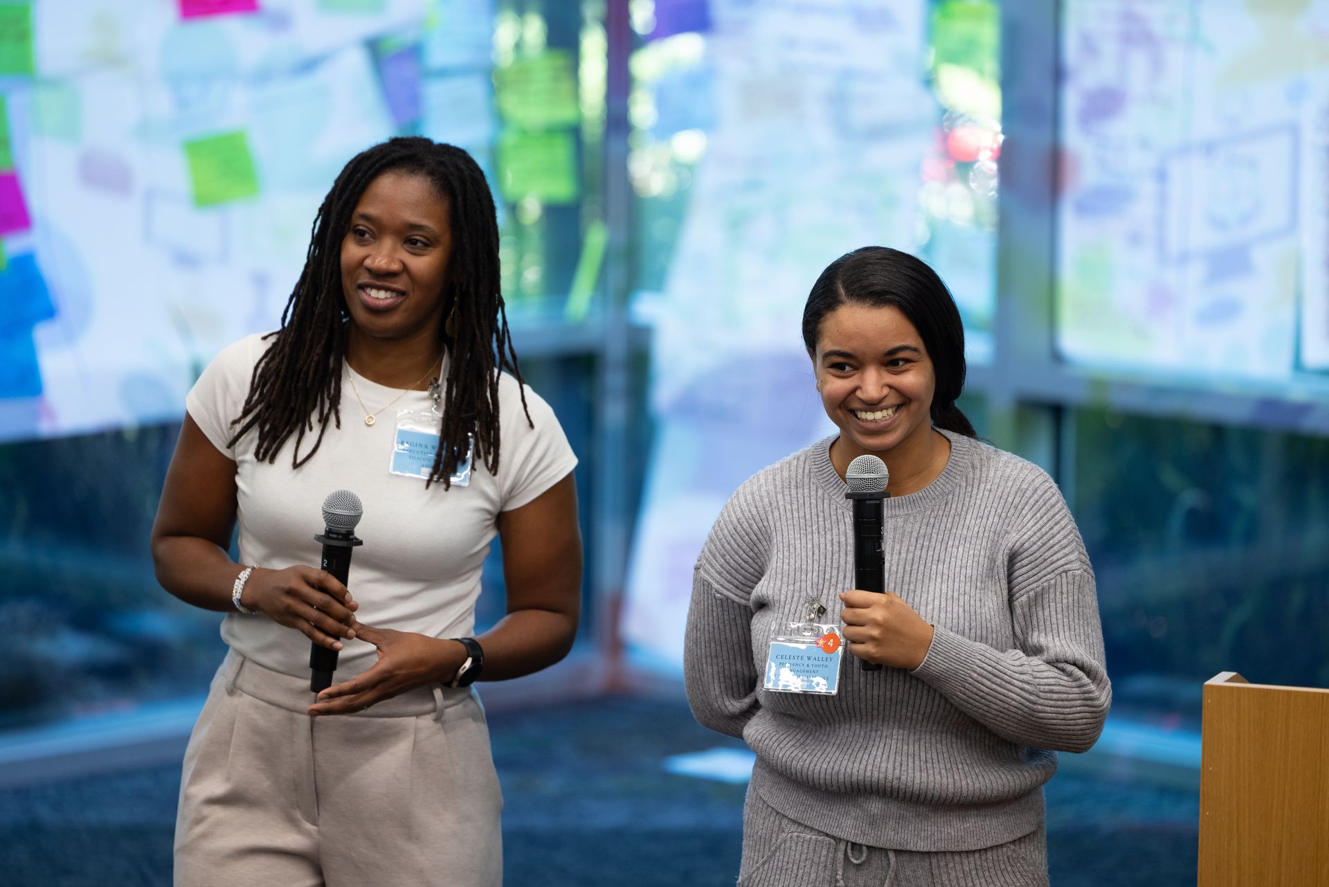 Two people holding microphones on a stage, smiling during a presentation.