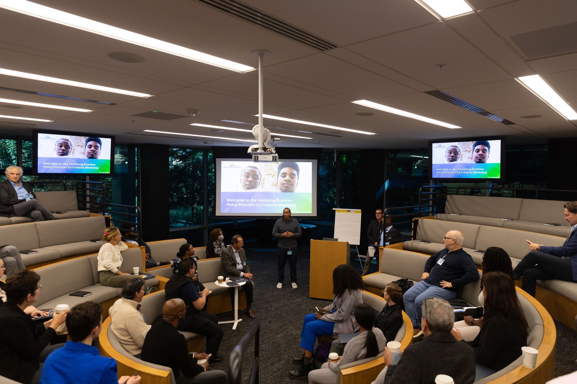 People seated in a modern conference room watching a presentation on multiple screens.