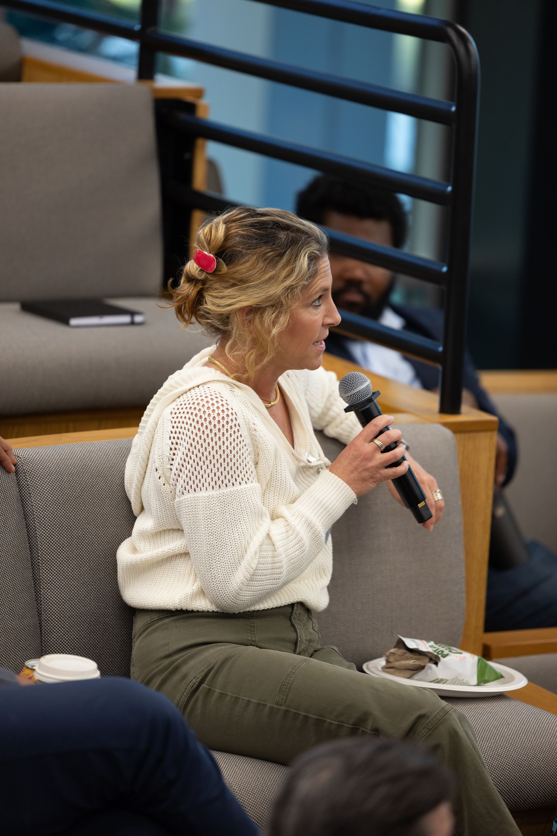 Woman speaking into a microphone on a couch at a seated event