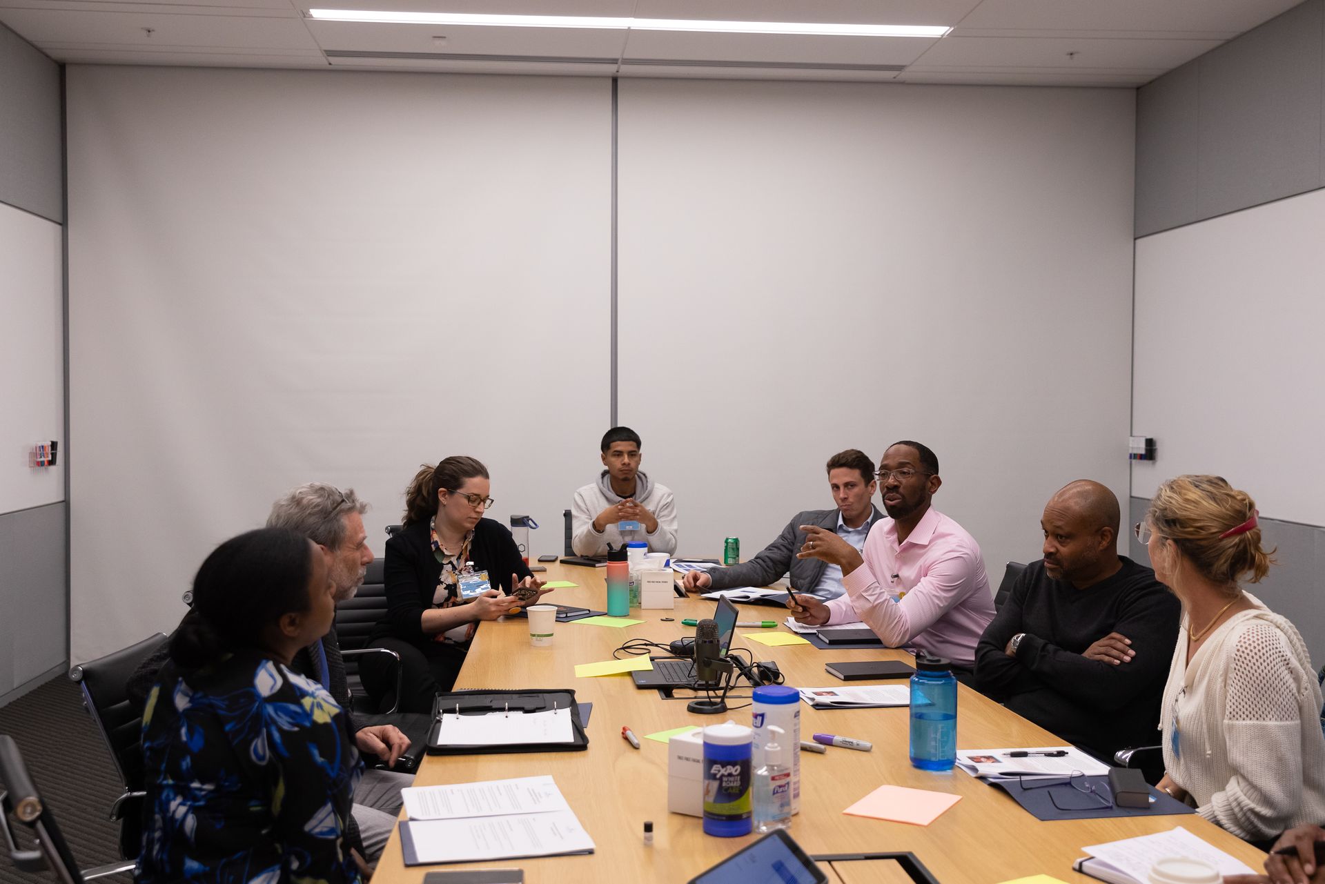 People seated around a conference table in a meeting room, with papers, laptops, and drinks.