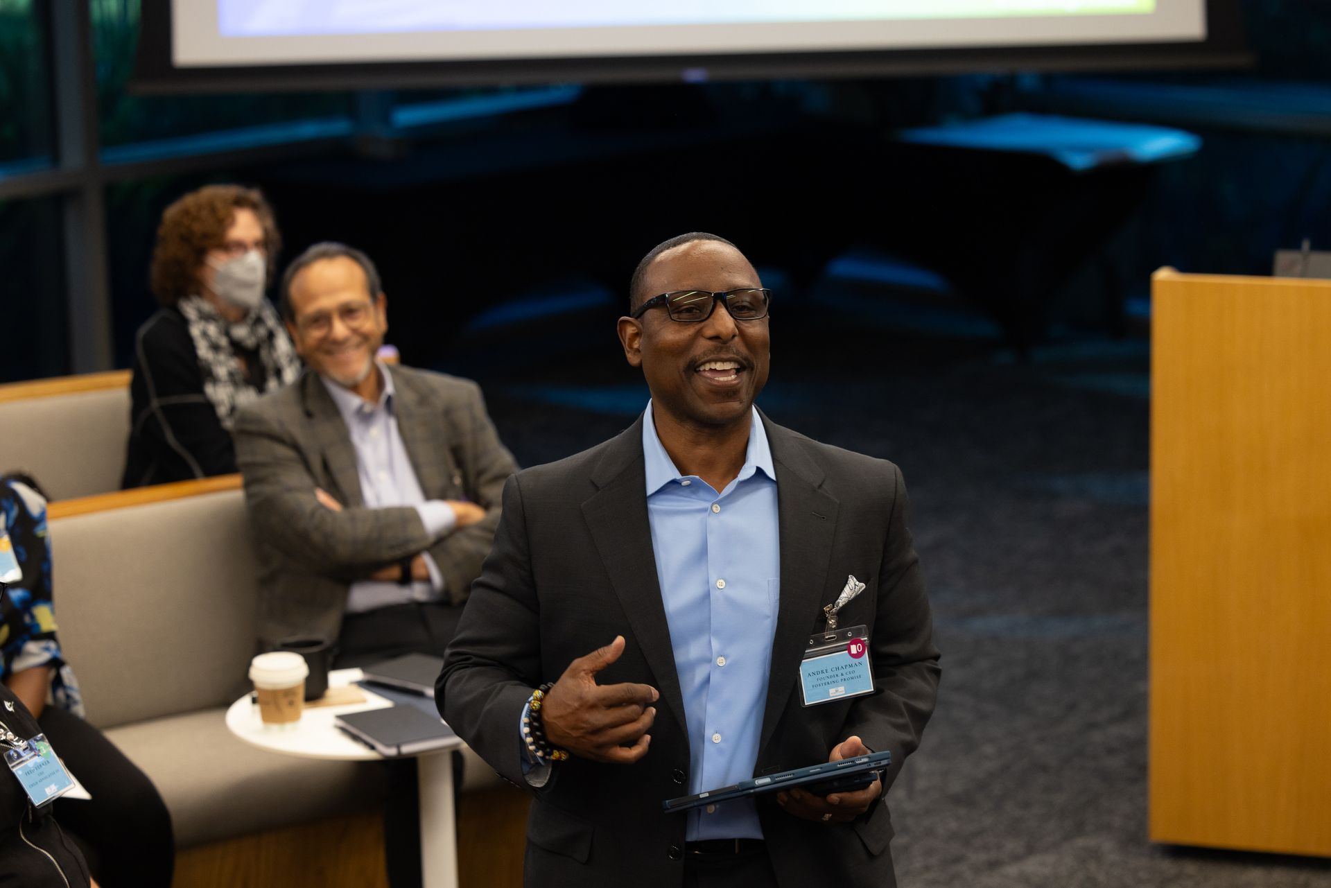 Man speaking at a conference while seated attendees listen in the background