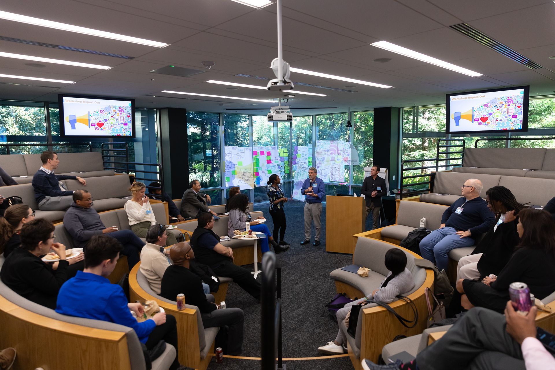 People seated in a modern meeting room watching a presentation on screens at the front.