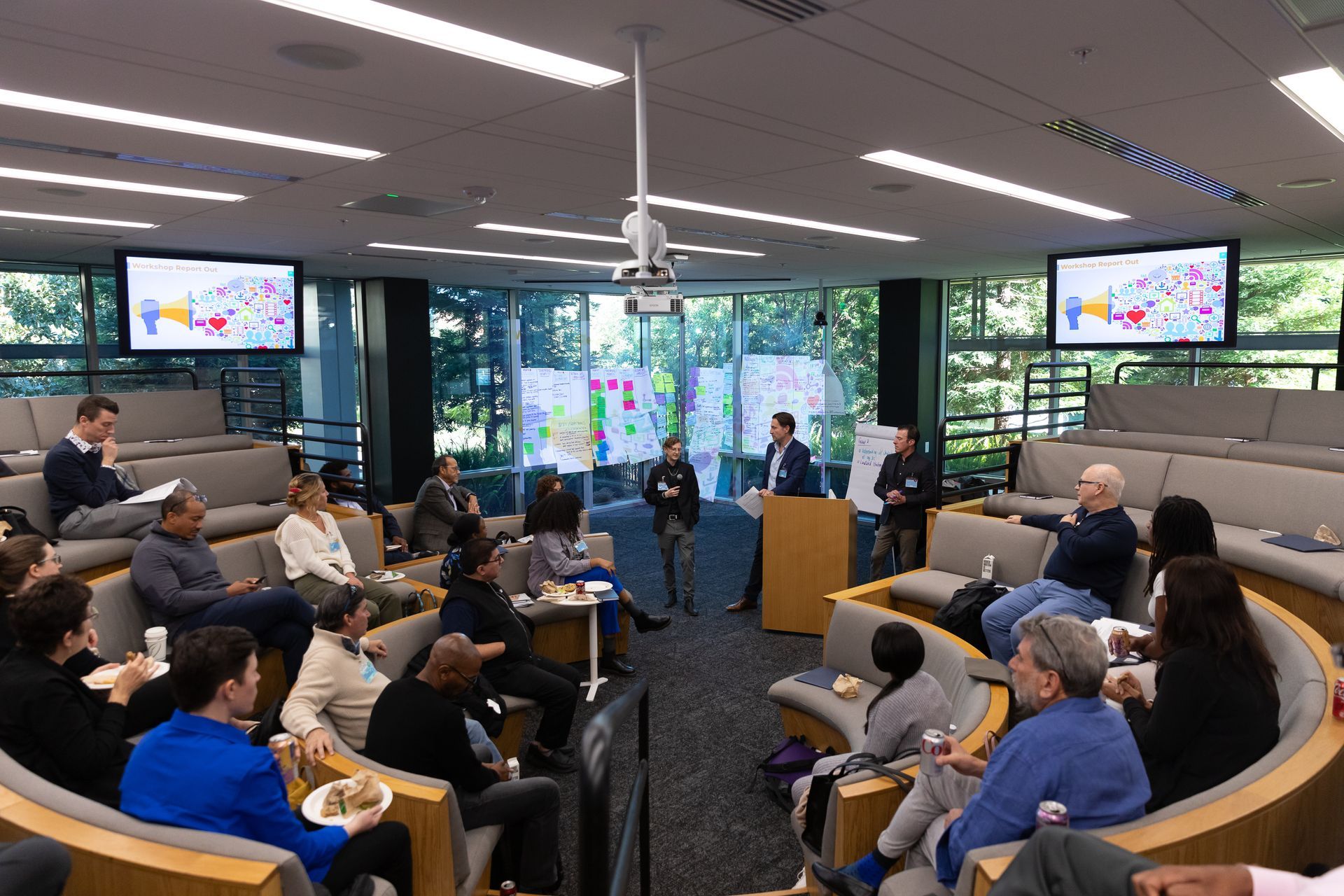 Meeting room with seated audience watching a presentation on multiple wall screens