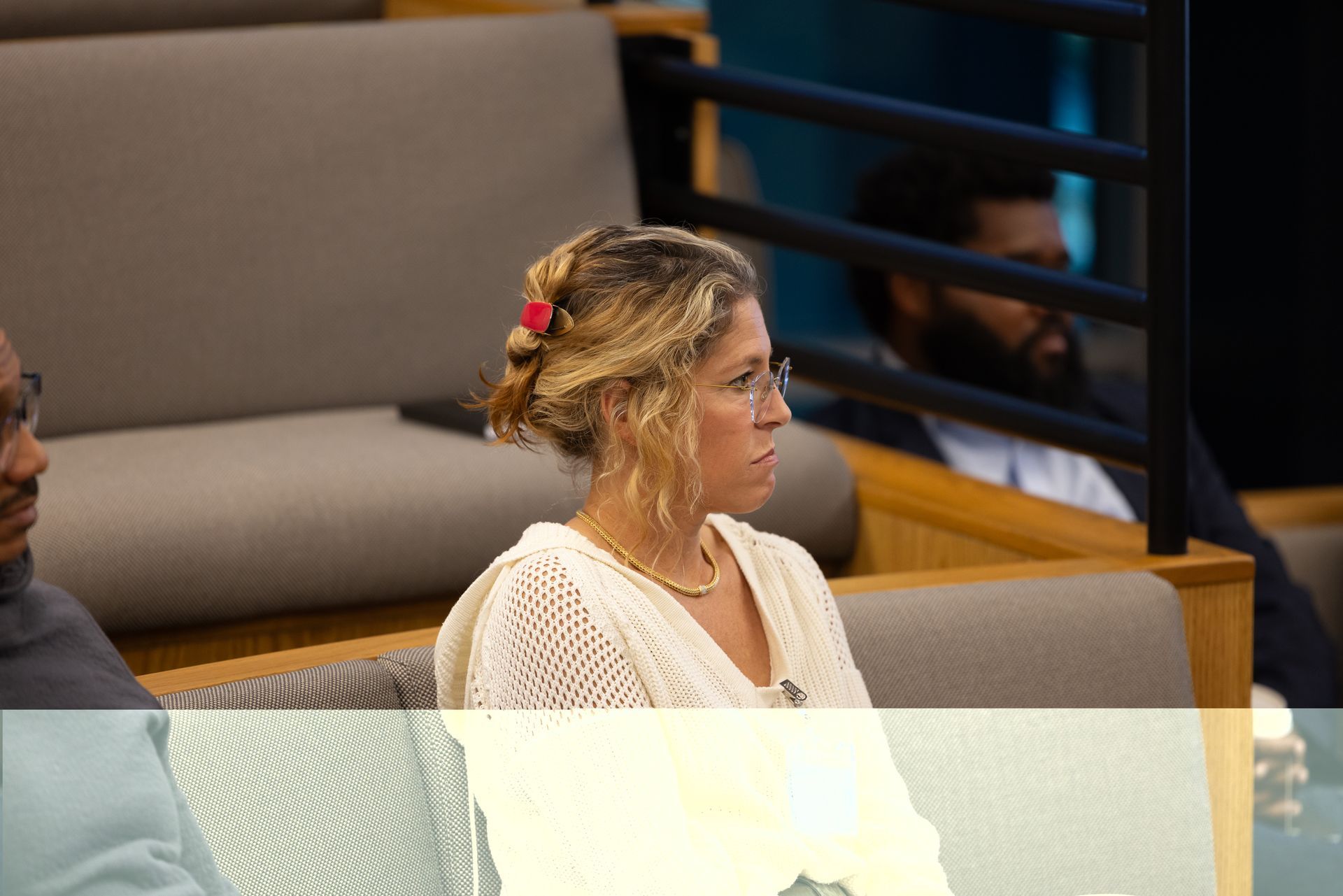 Woman seated in a church pew, wearing a white sweater and looking to the side.