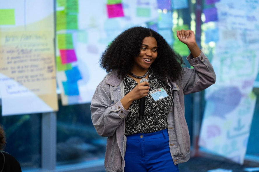 Woman smiling and raising a fist in front of colorful notes and posters on a wall