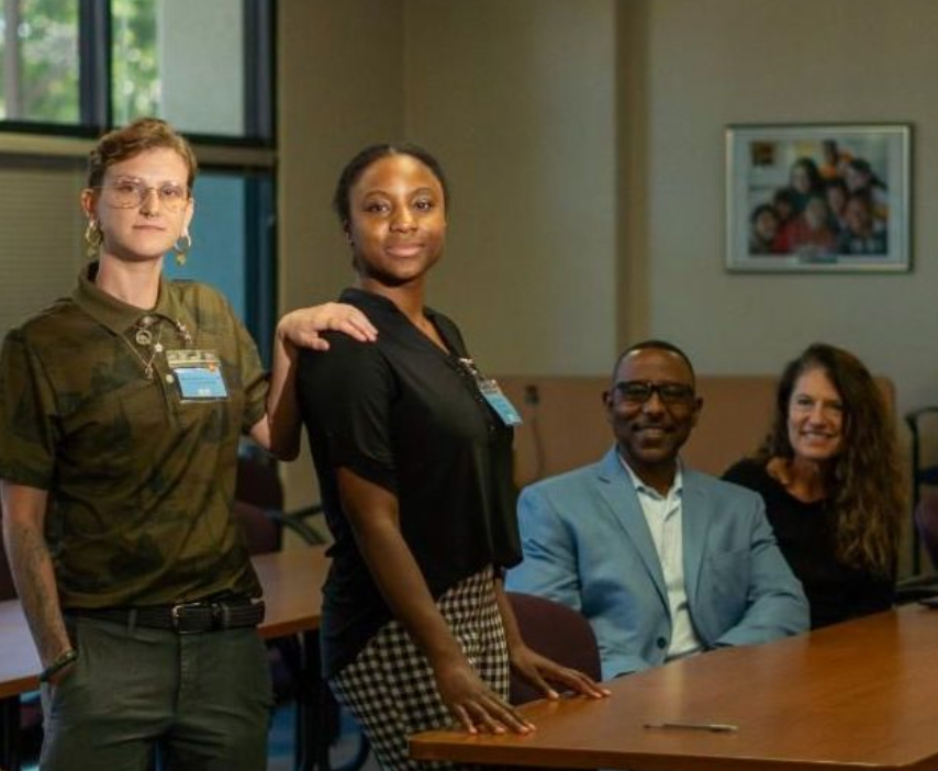 Four colleagues pose in a conference room around a meeting table, smiling at the camera.