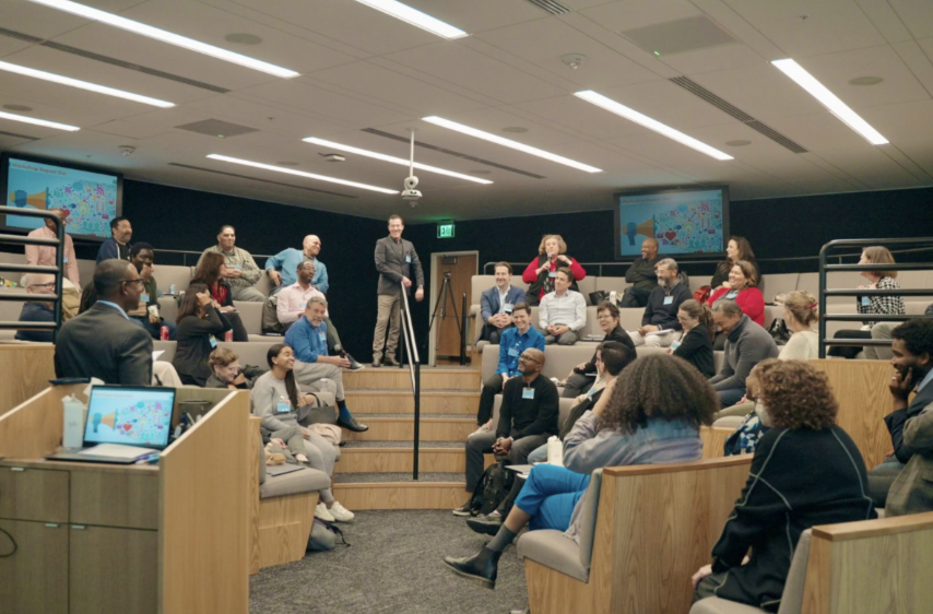 Audience seated in a lecture hall listening to a speaker at the front of the room.