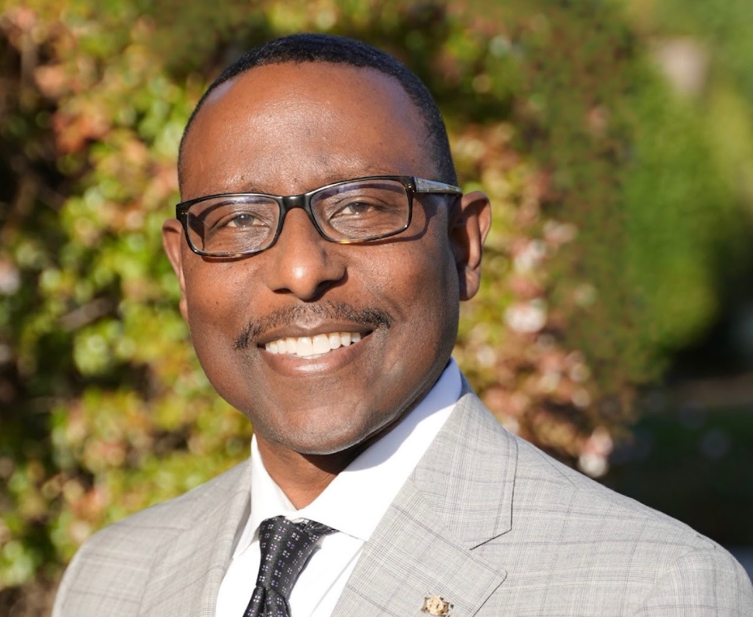 Smiling man in glasses and light gray suit outdoors in sunlight