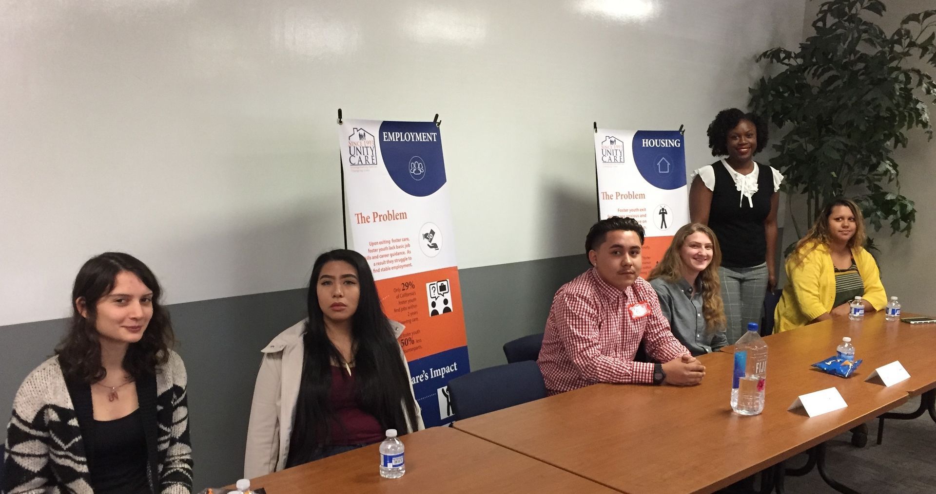 Panelists seated at a conference table in a meeting room, with posters on the wall behind them.
