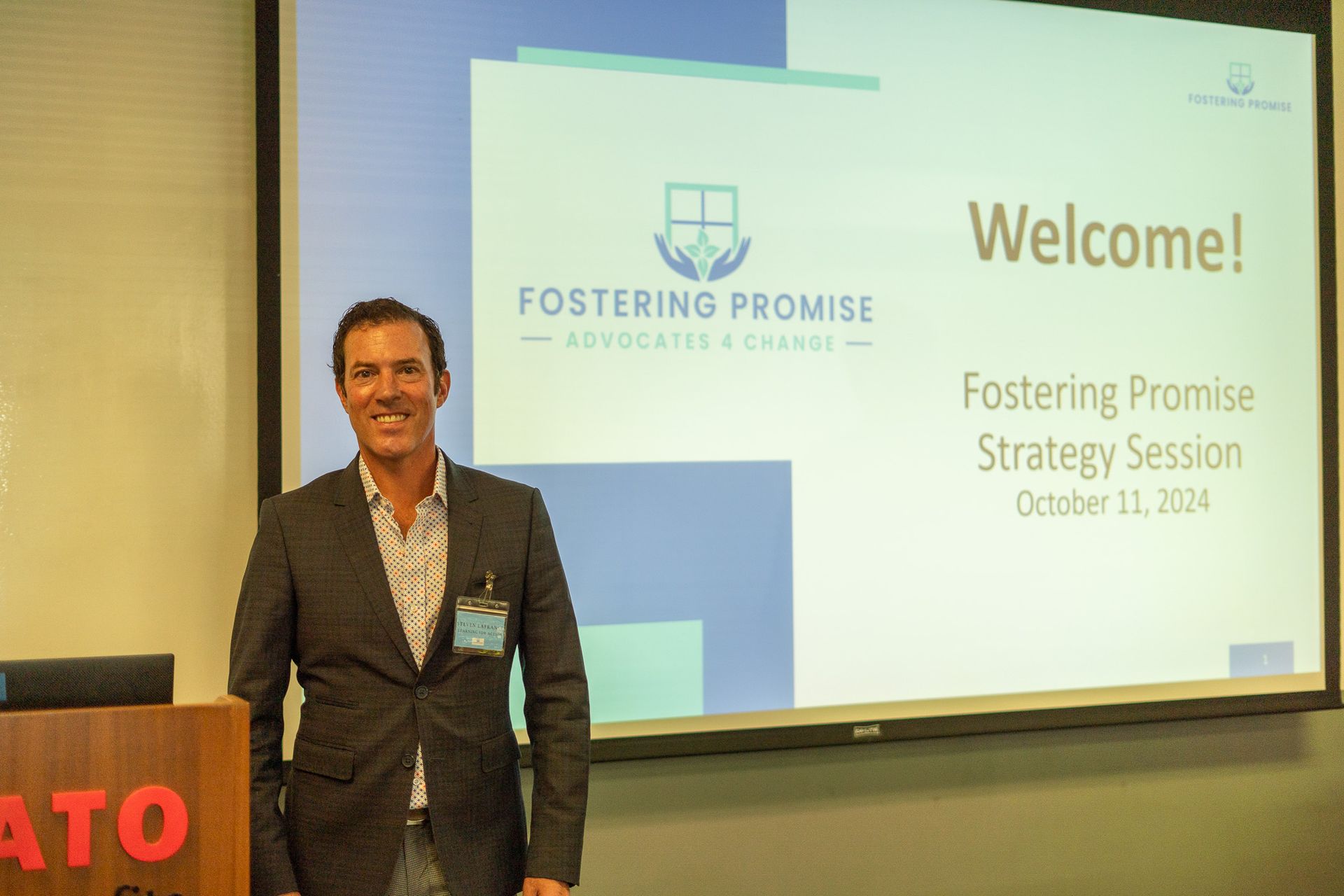 Man standing beside presentation screen reading “Welcome! Fostering Promise Strategy Session”