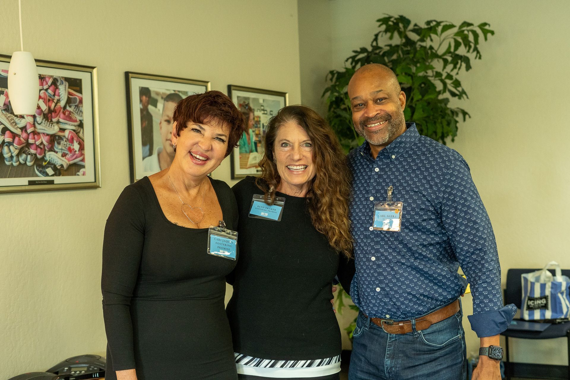 Three smiling people posing indoors in a room with framed art on the wall.