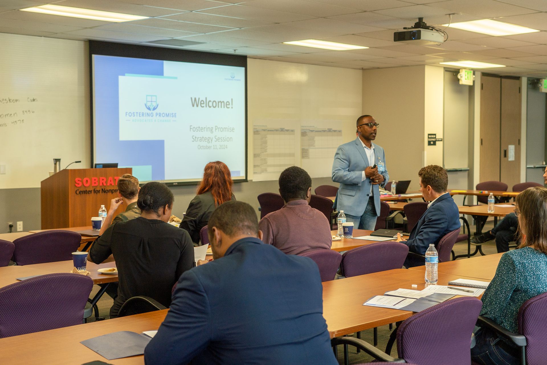 Classroom presentation with seated attendees facing a projected “Welcome!” slide in a lecture room