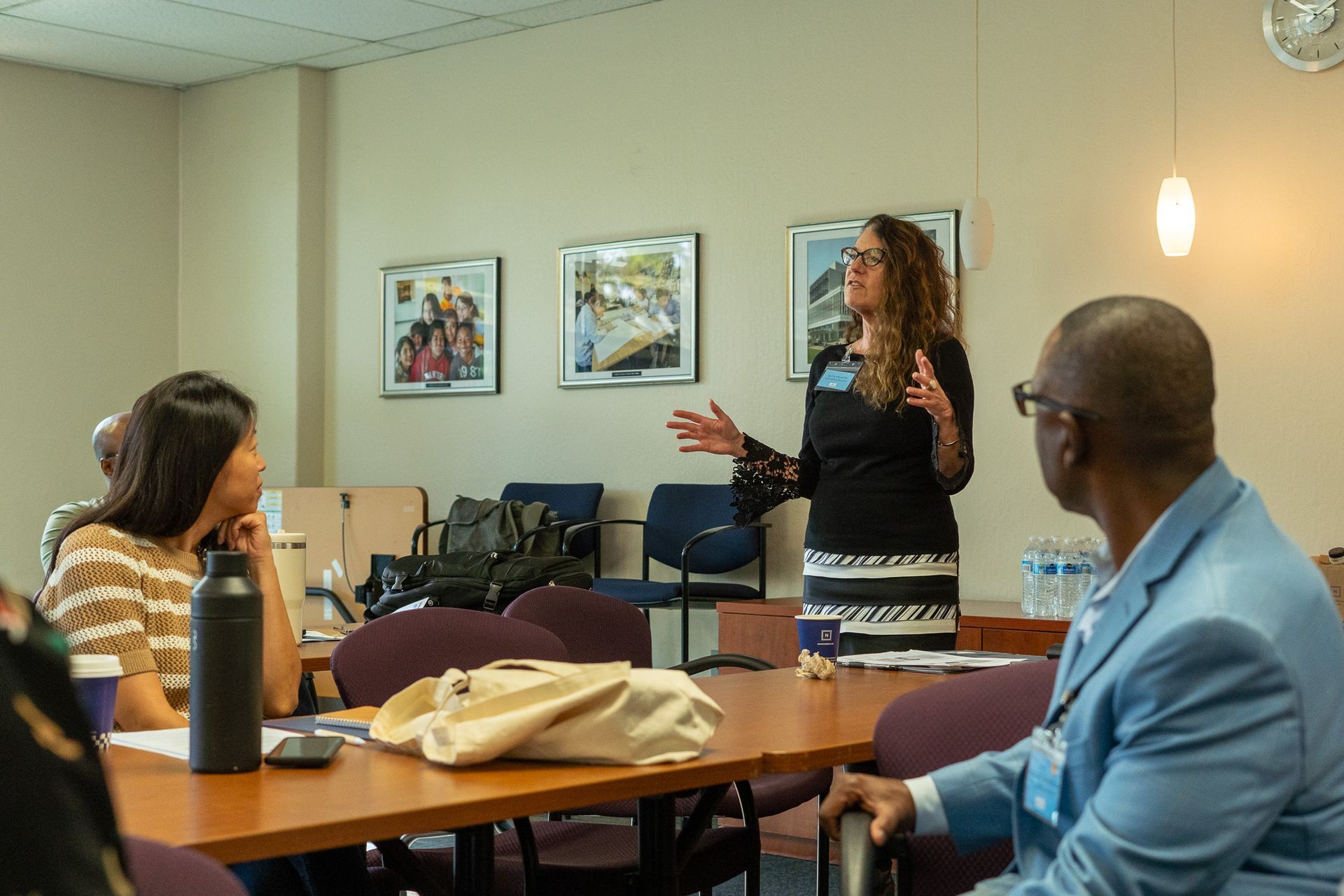 Small meeting room with three people discussing a presentation near a table and projector equipment.