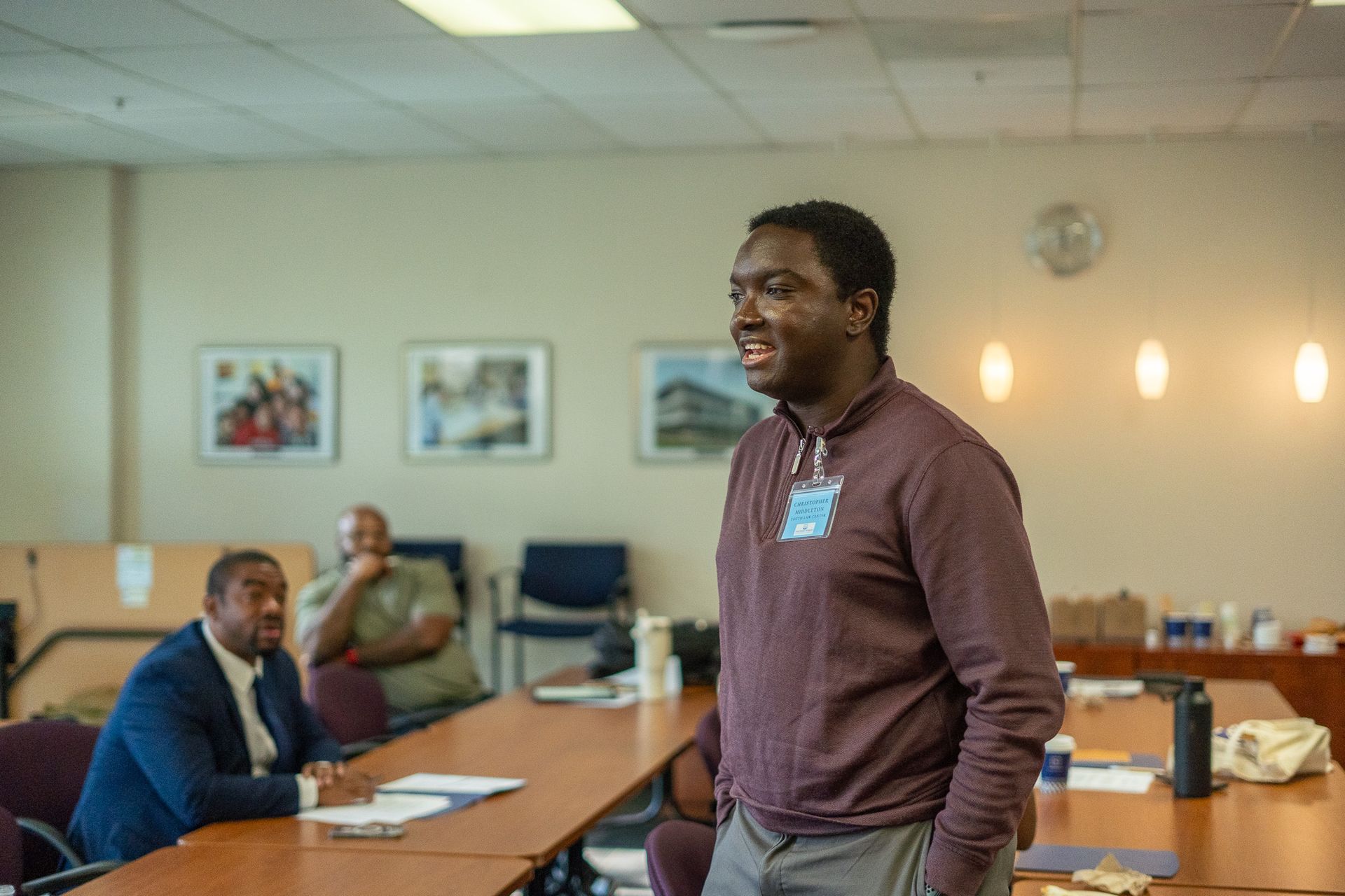 Man standing in a conference room with people seated at a table behind him.