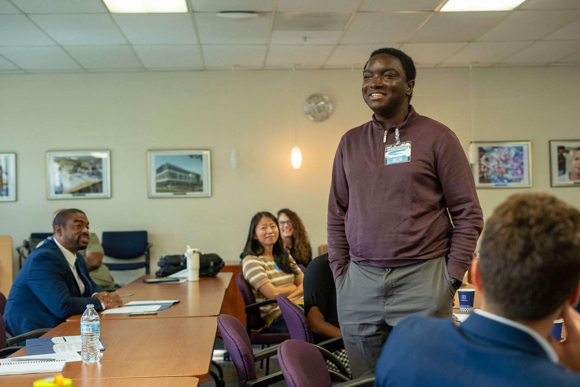 Meeting room with a standing presenter and seated attendees around a conference table