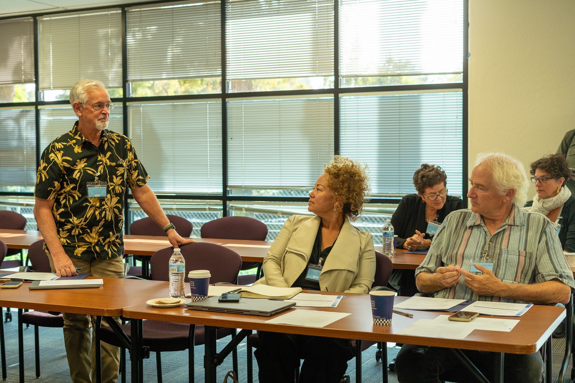 People seated at a meeting table while a man stands and speaks in a conference room.