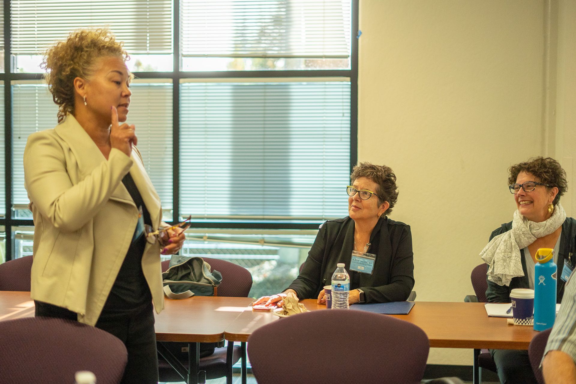 Presenter speaking to two seated attendees in a classroom or meeting room.