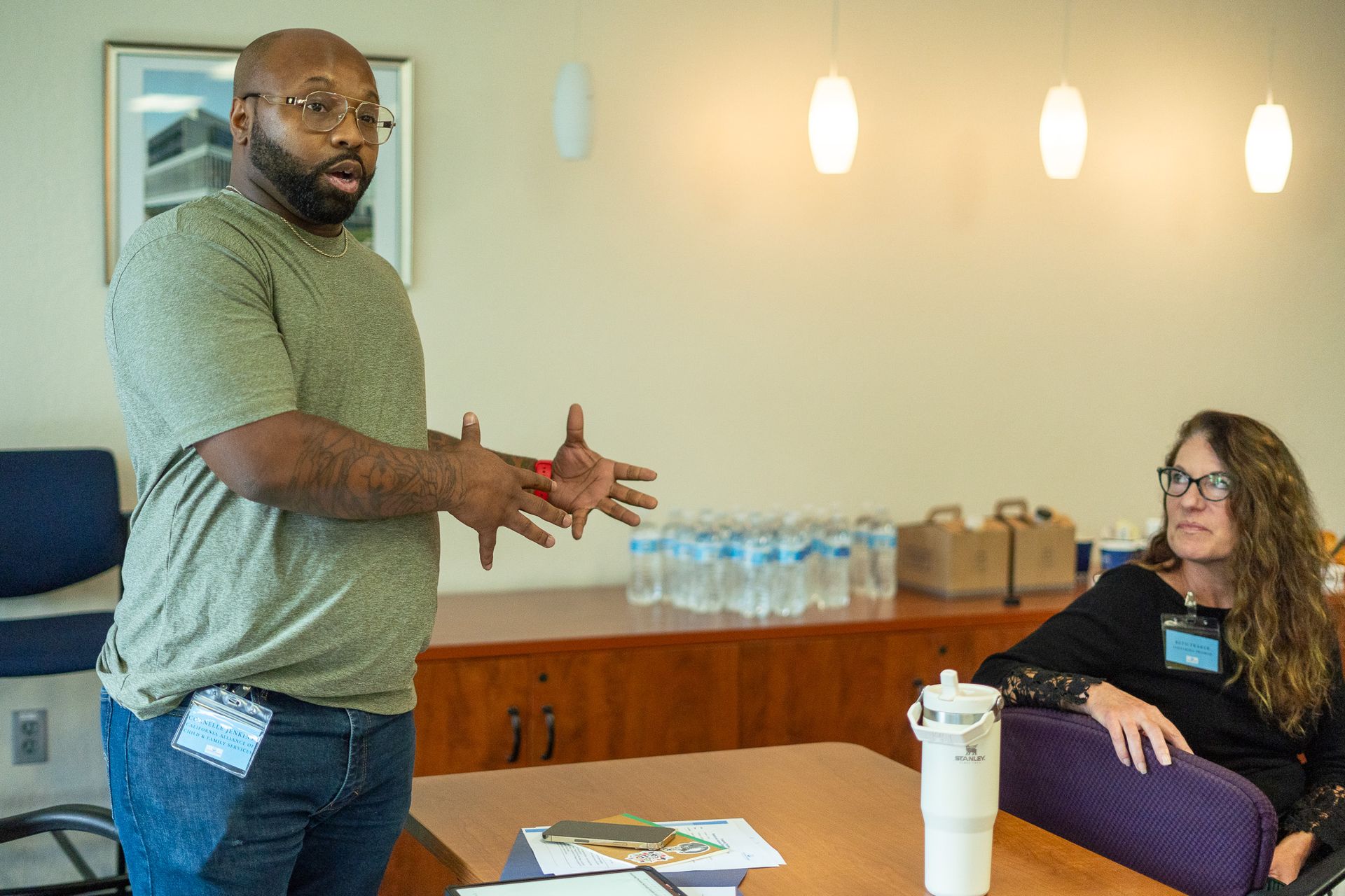Two people talking in an office, with water bottles and papers on a table.