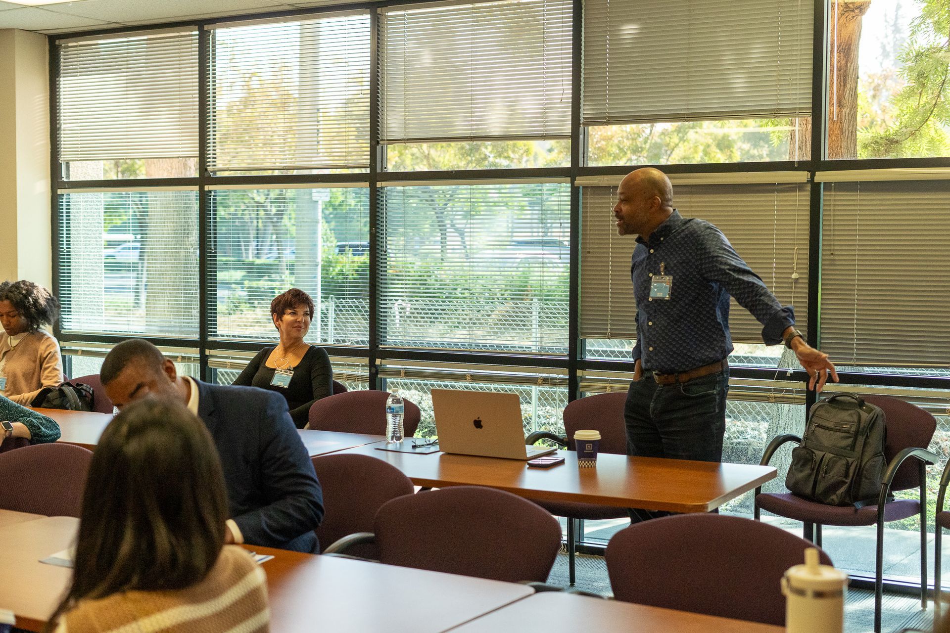 People seated in a bright conference room while a presenter stands beside a laptop and table.