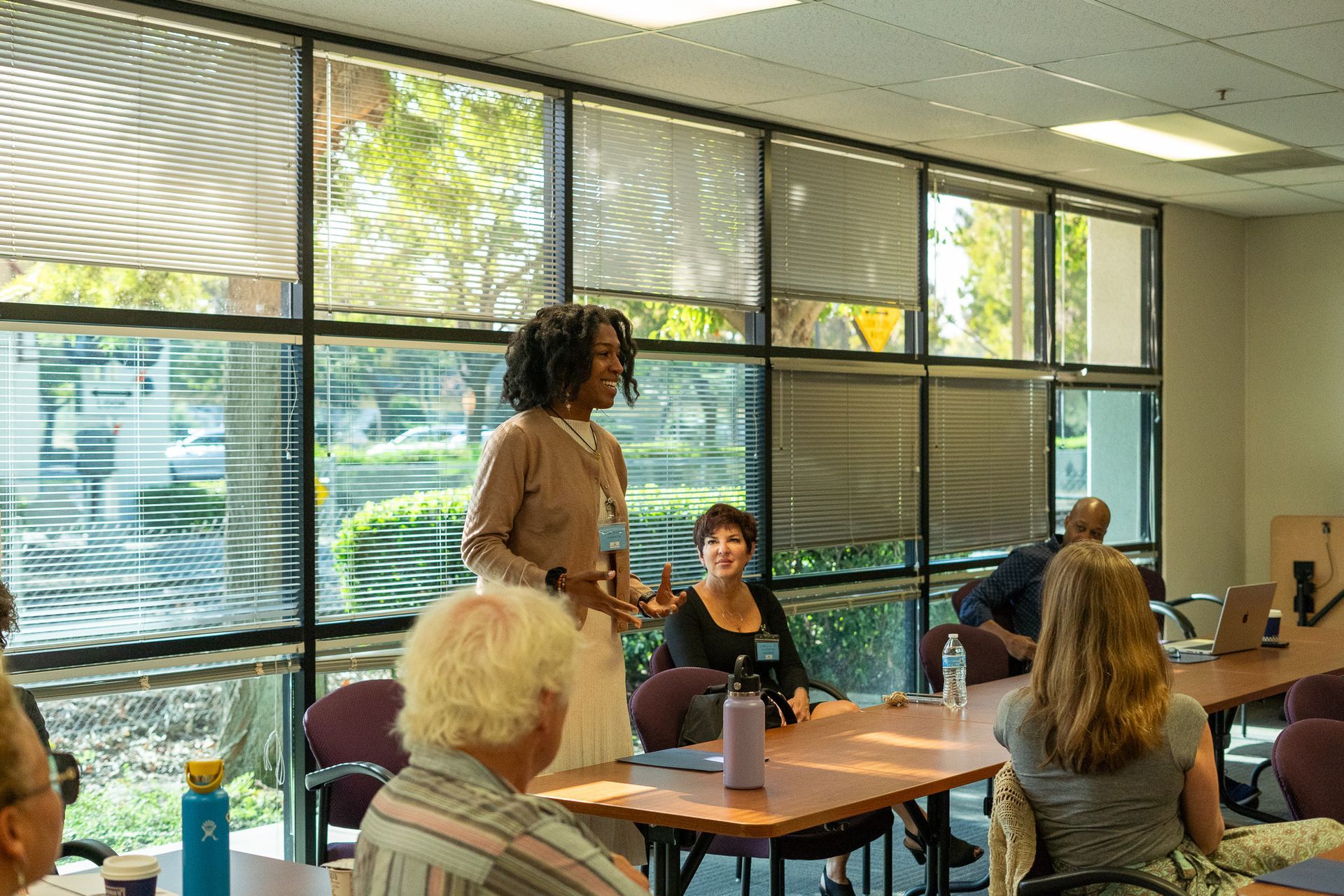 People gathered in a bright meeting room, with one speaker standing near large windows.