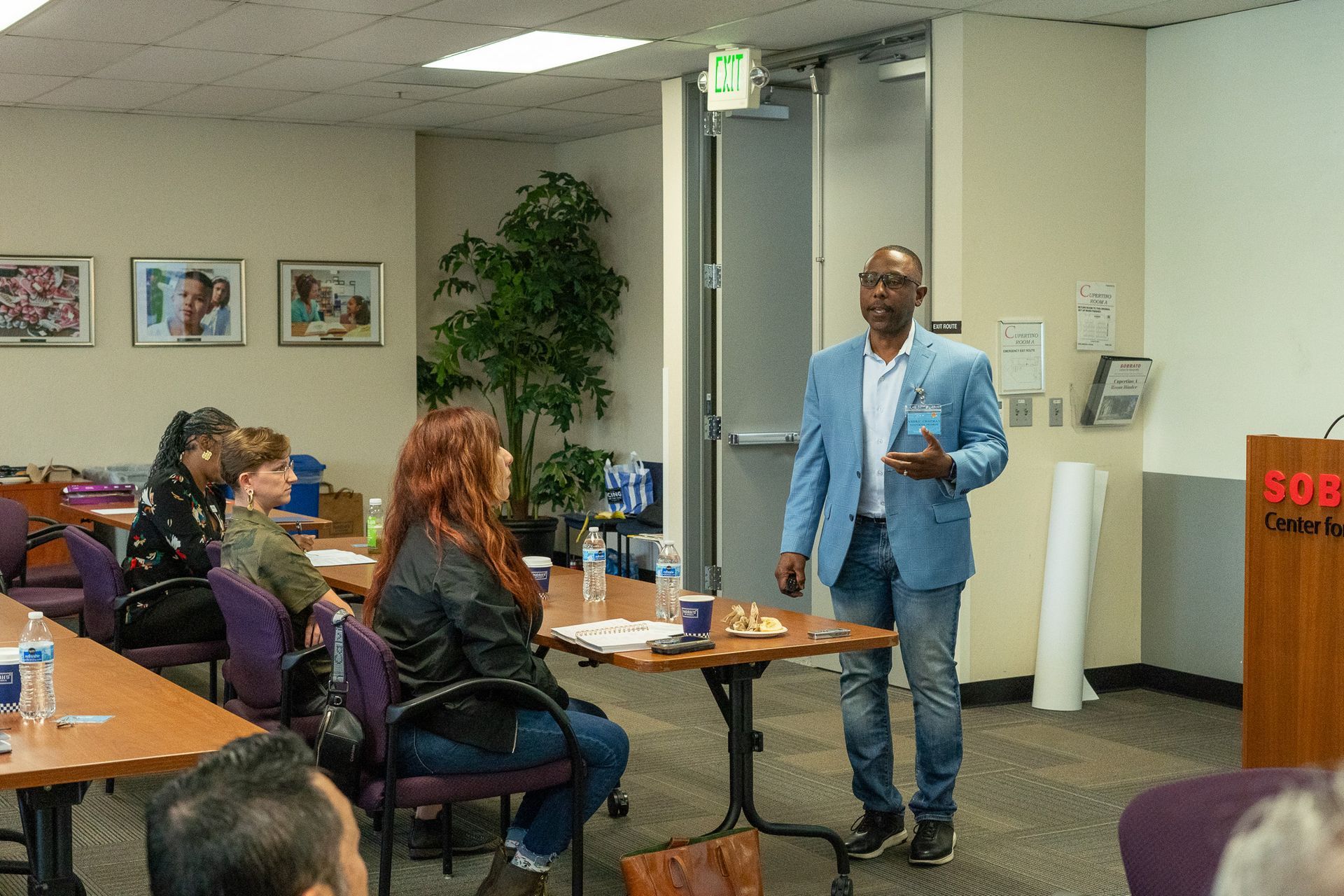 Man in a light blue blazer speaking to seated audience in a small conference room