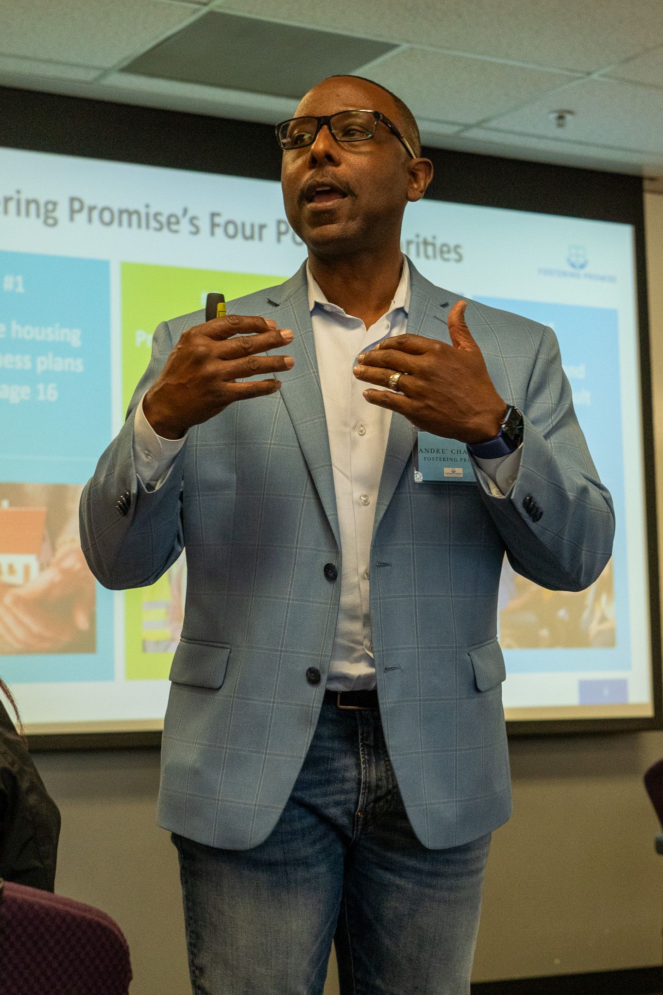 Man speaking in a blue blazer in front of a projected presentation screen