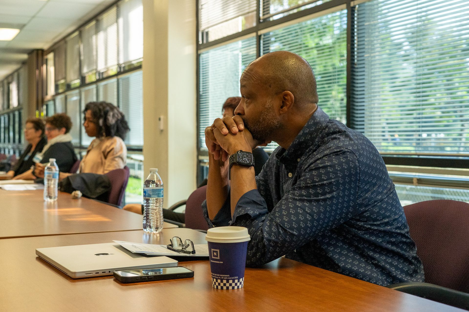 People seated at a conference table in a bright meeting room, listening attentively.