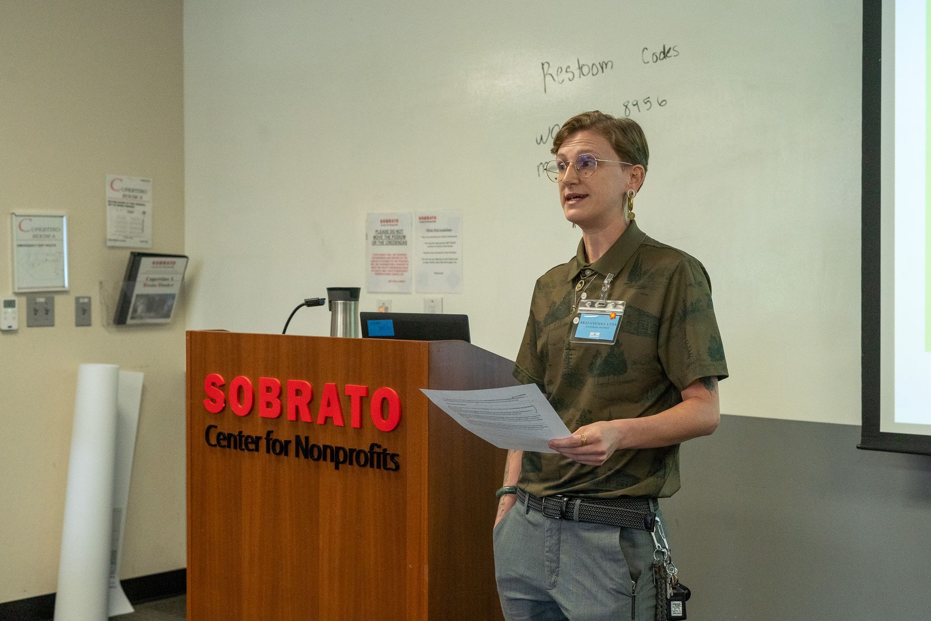 Speaker at a podium labeled “Sobrato Center for Nonprofits,” holding papers during a presentation.