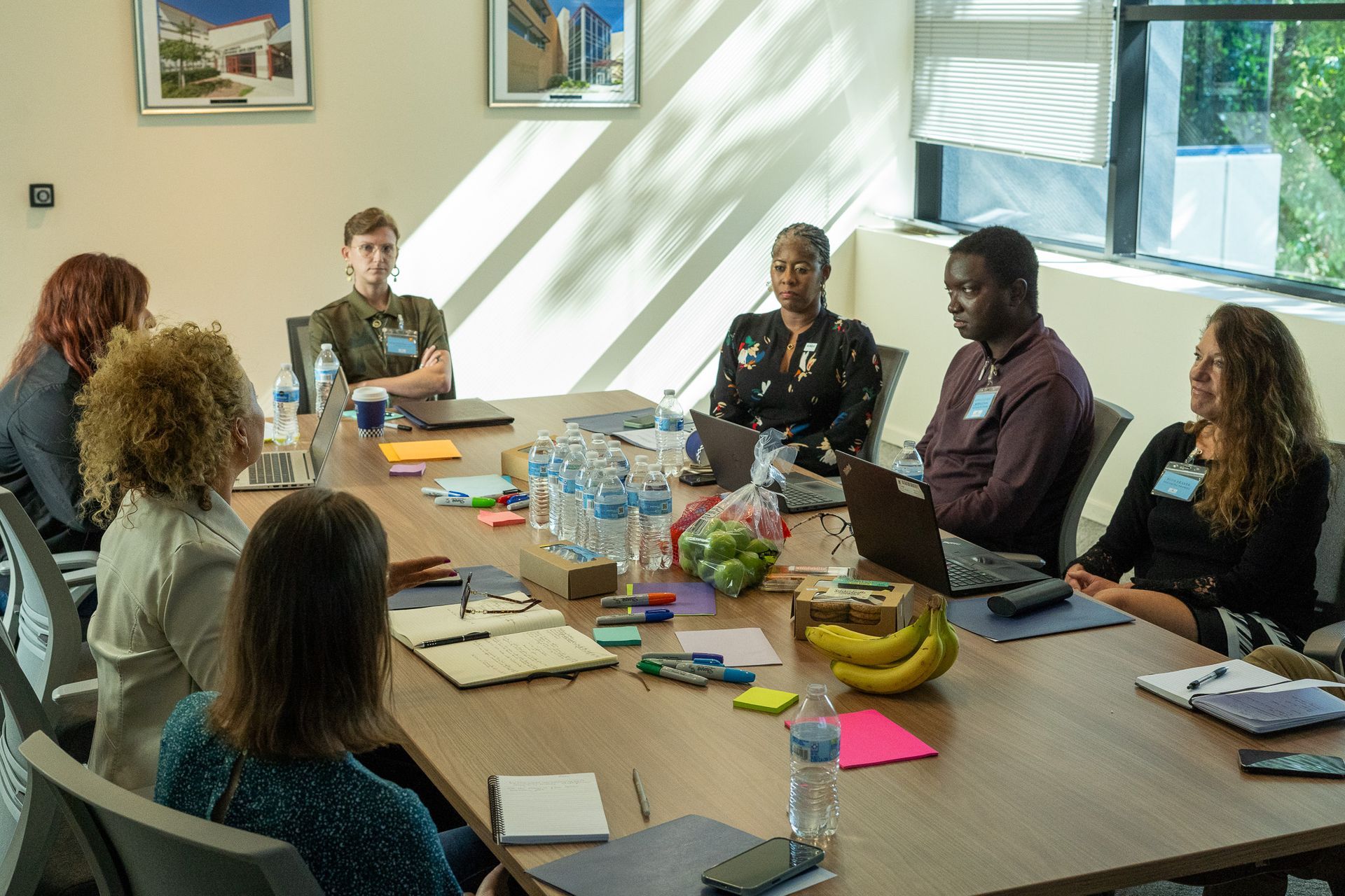 People seated around a conference table in a bright meeting room, discussing with laptops and notes.