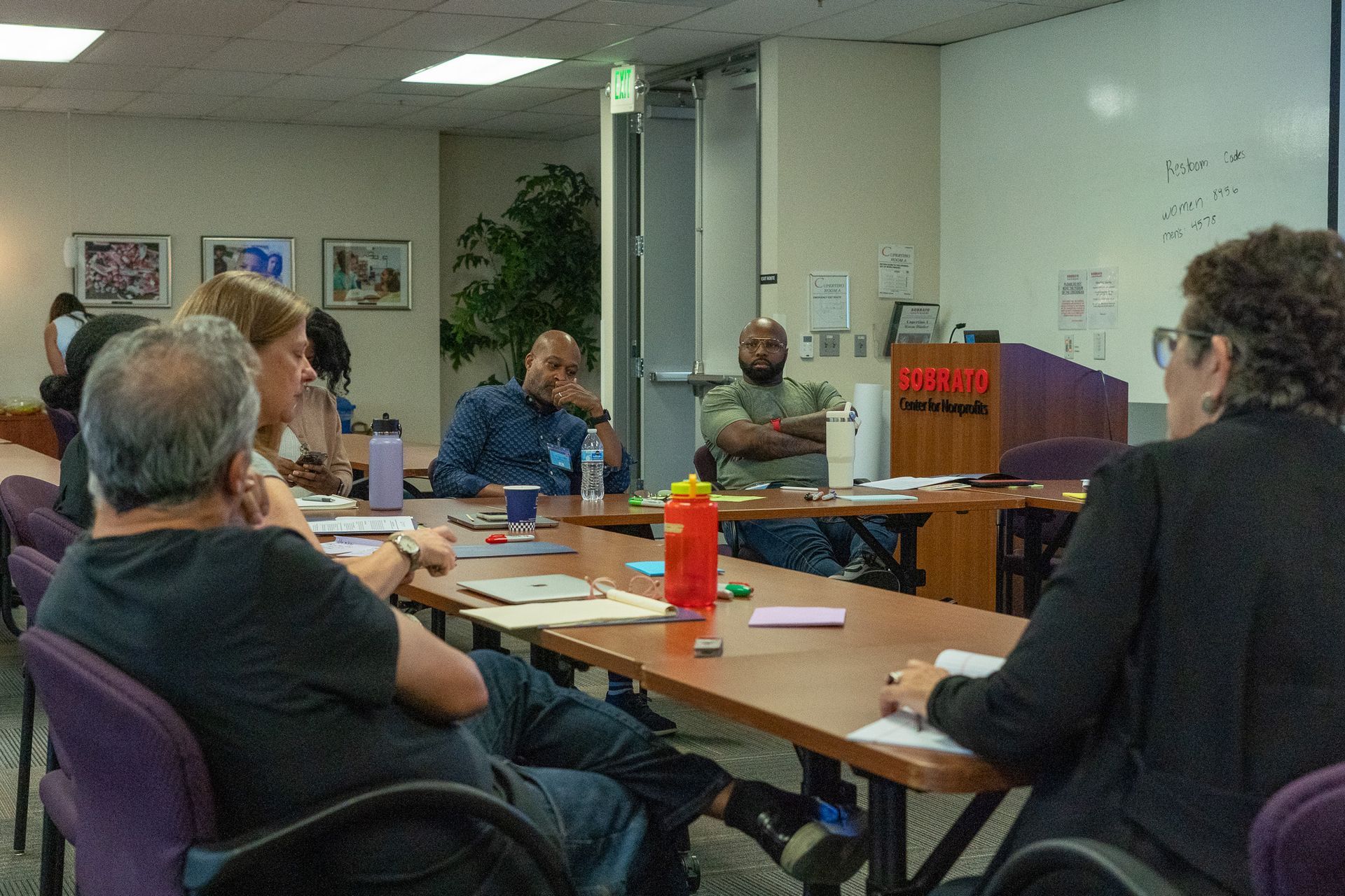 Small group meeting around a conference table in a meeting room, with papers, bottles, and a podium.
