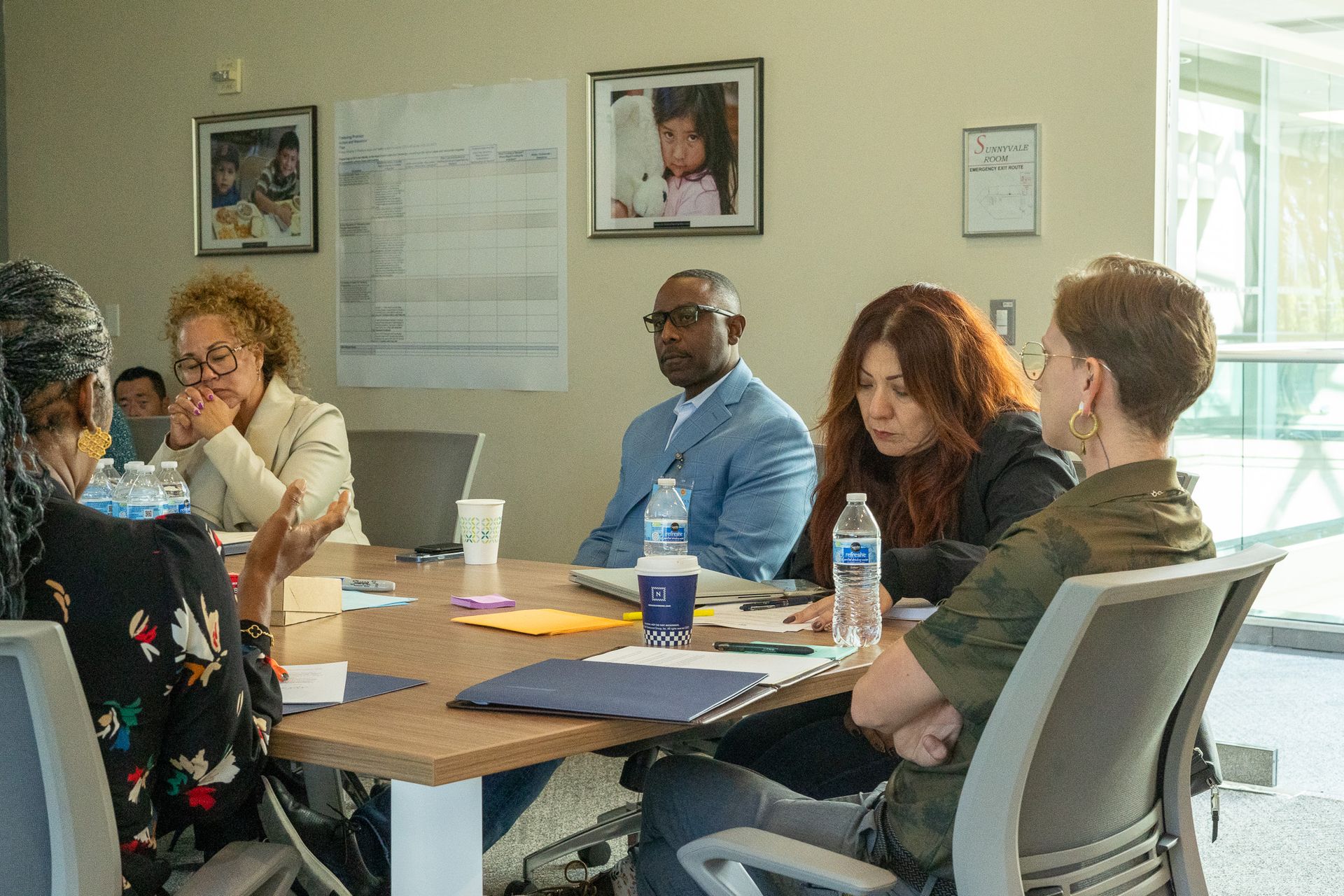 Several people sit around a conference table in a meeting room, talking and taking notes.