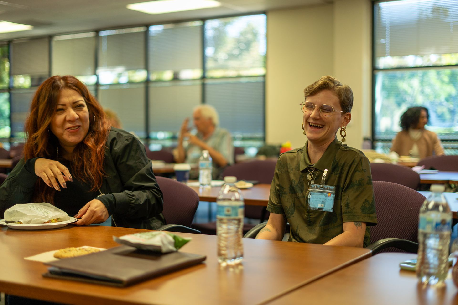 People seated at a conference table in a meeting room, smiling and talking with papers and water bottles nearby
