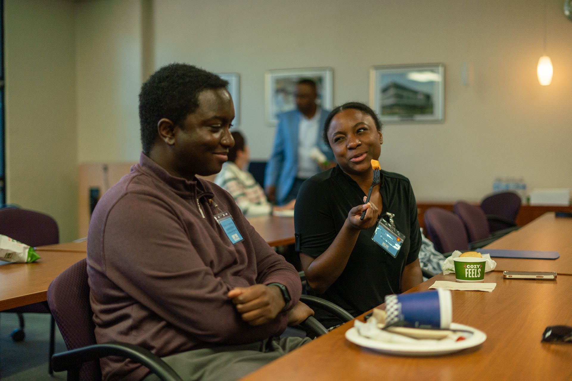 Two people sit at a conference table, one speaking while the other listens.